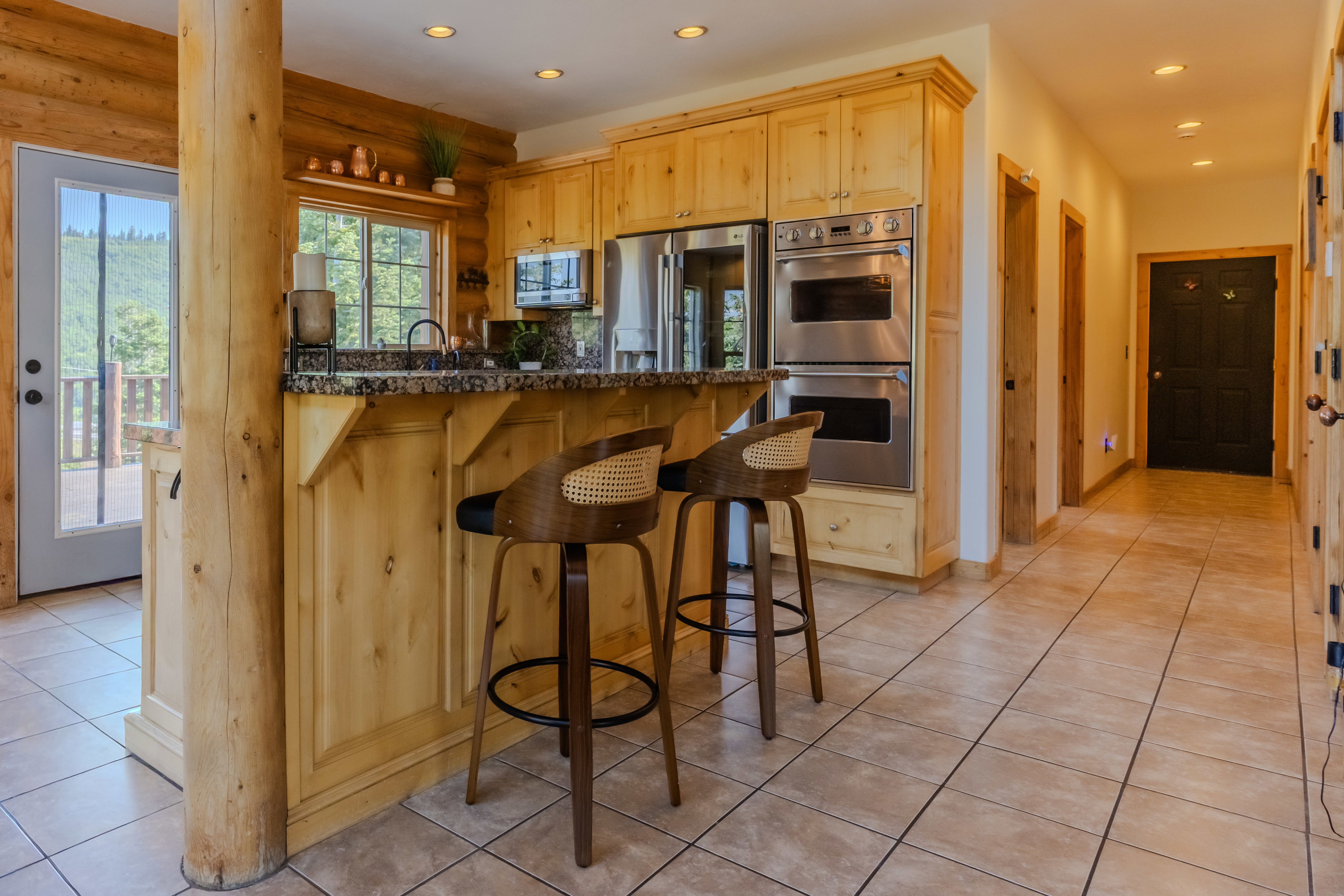 Open kitchen area featuring granite countertops, wood cabinetry, stainless steel double ovens, and tile flooring
