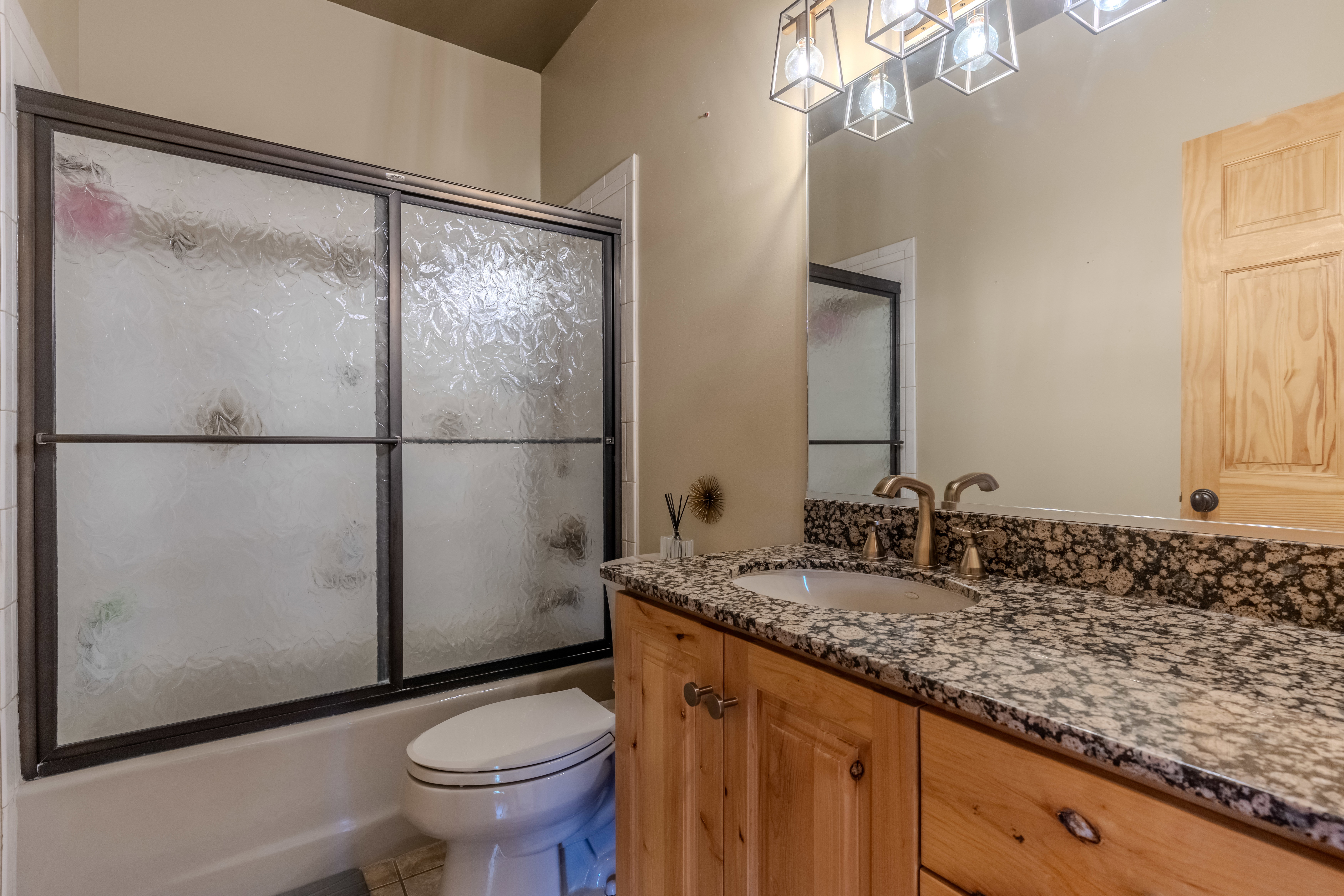 Bathroom featuring a granite-look vanity with an undermount sink, a wood-finish cabinet, and a metallic light fixture