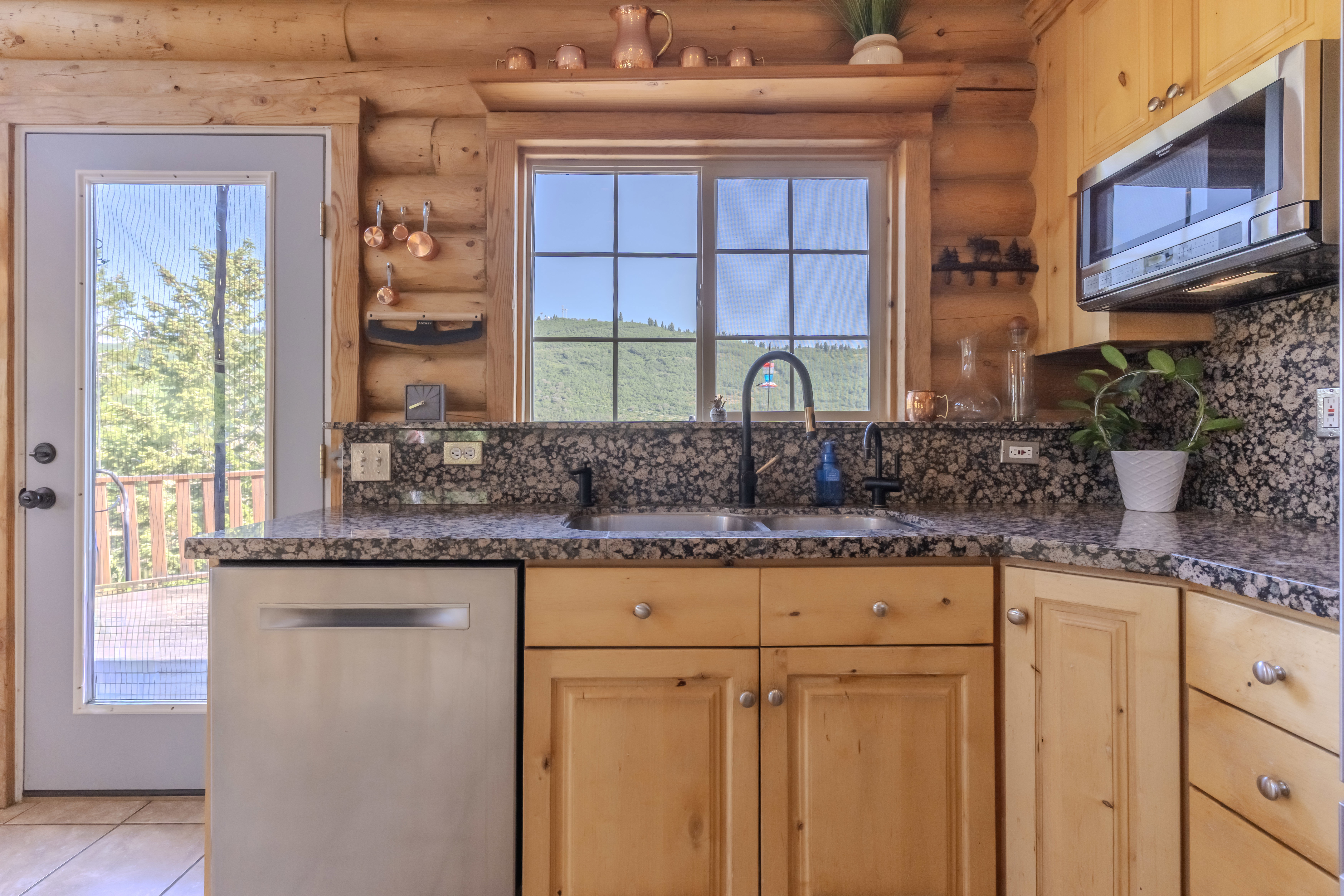 Kitchen featuring a double basin sink with a matte black faucet, granite countertops, wood-finish cabinetry, a stainless steel dishwasher, and an over-range microwave