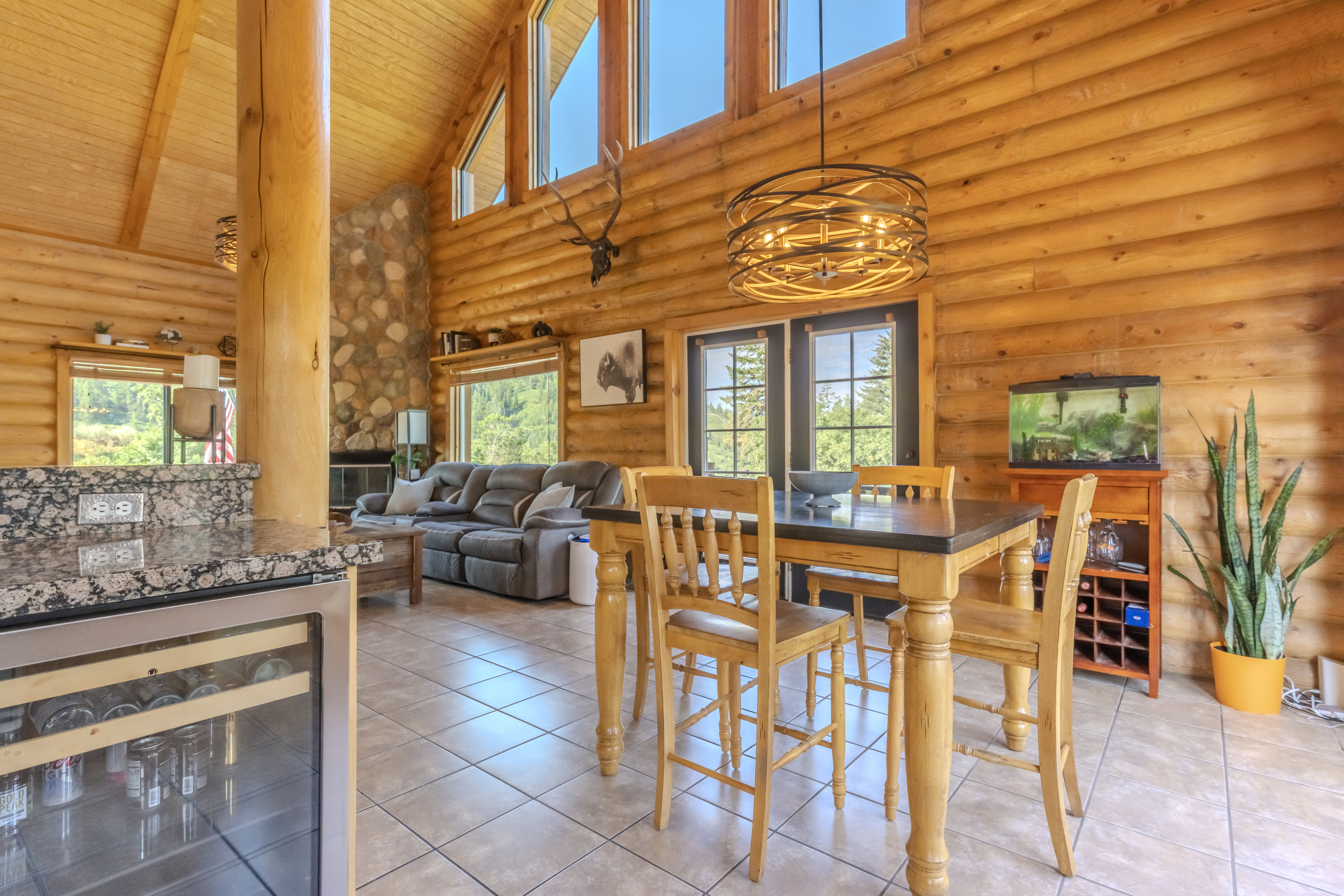 Open-concept living space with log walls, vaulted wood-plank ceilings, and large picture windows