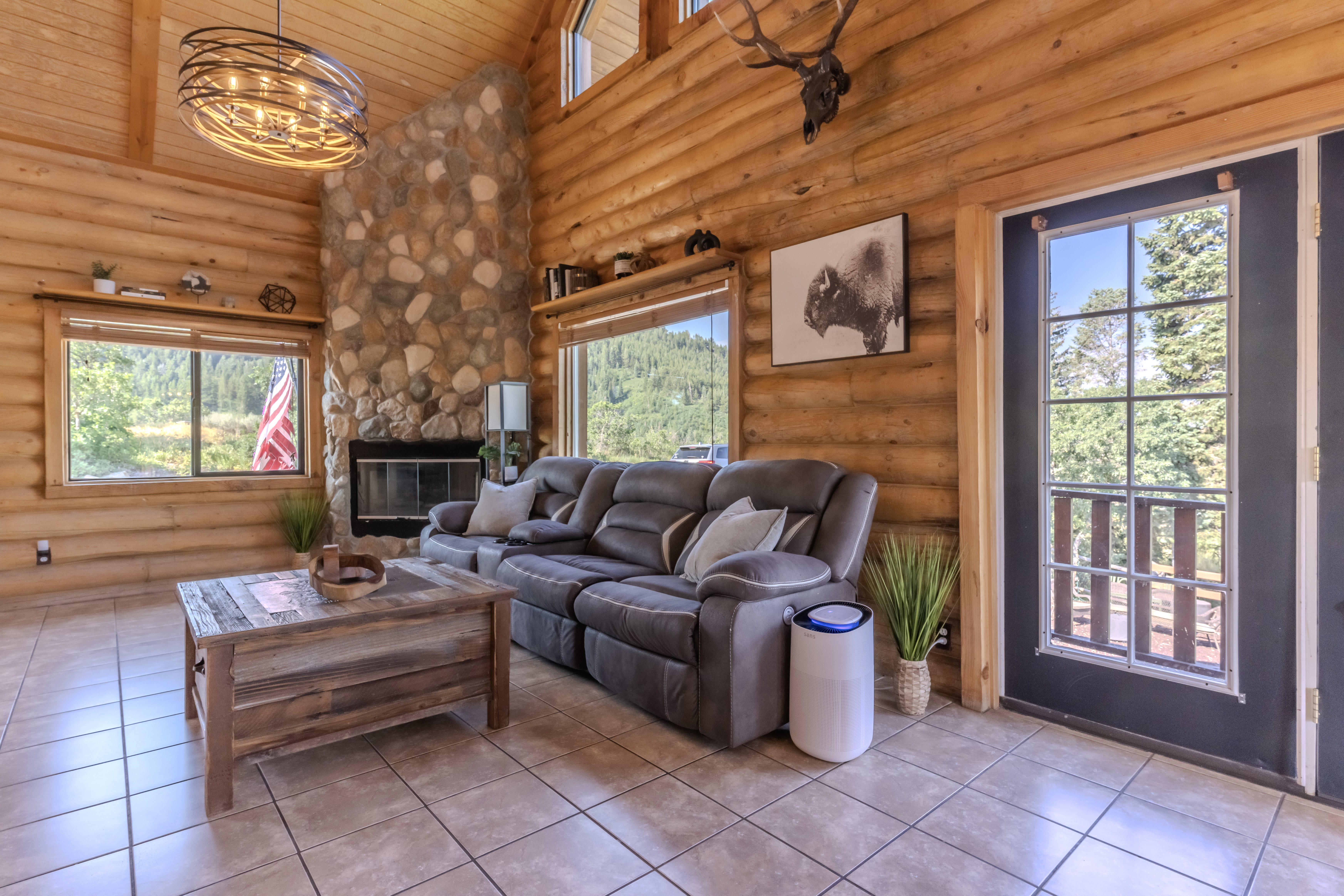 Log cabin interior featuring a stone fireplace, exposed wood log walls, vaulted wood plank ceilings, and ceramic tile flooring