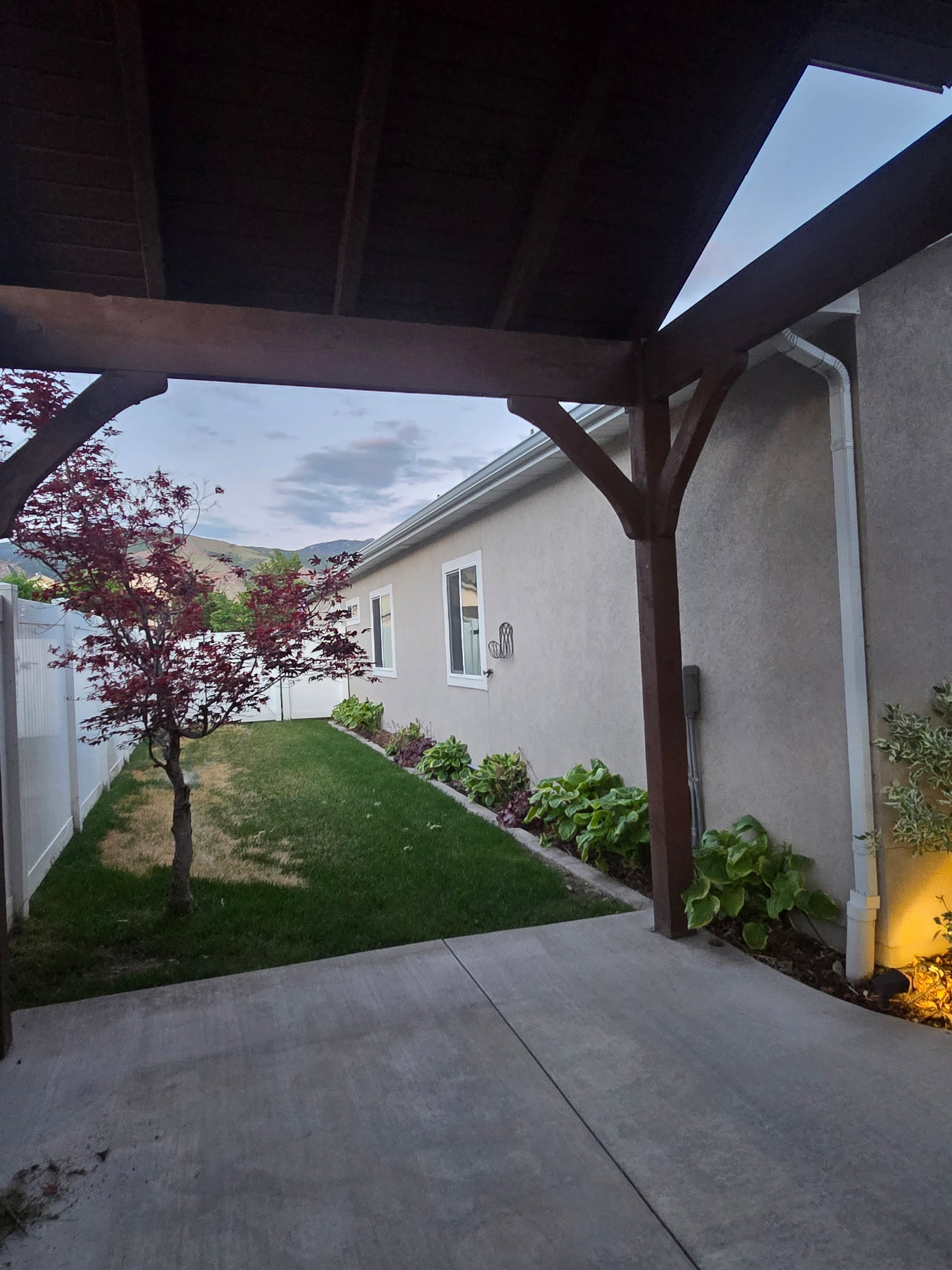Covered patio featuring a stained wood beam structure, concrete flooring, and surrounding landscaping