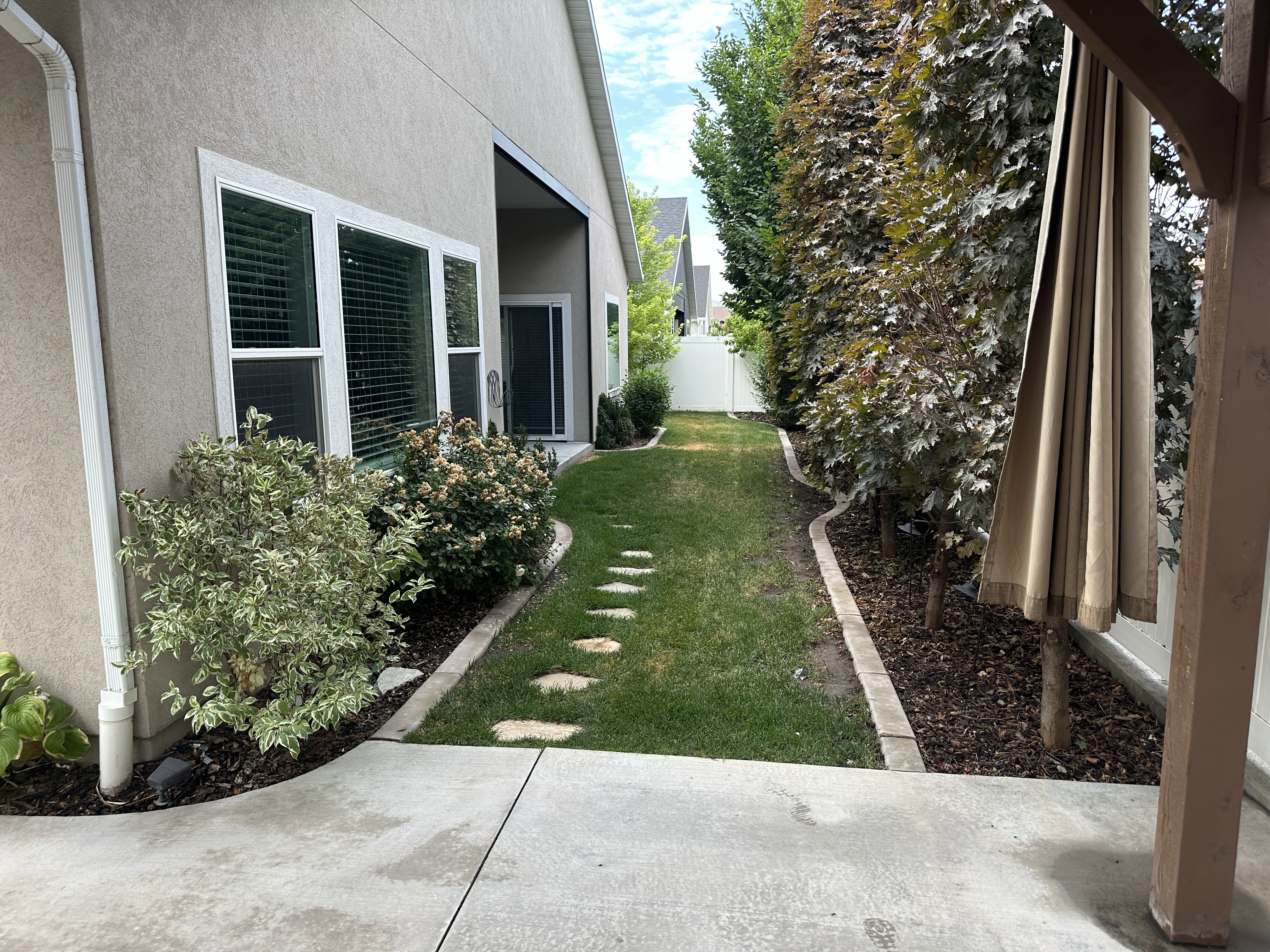 Lush side yard featuring a stepping stone pathway, manicured lawn, and mature trees providing natural screening