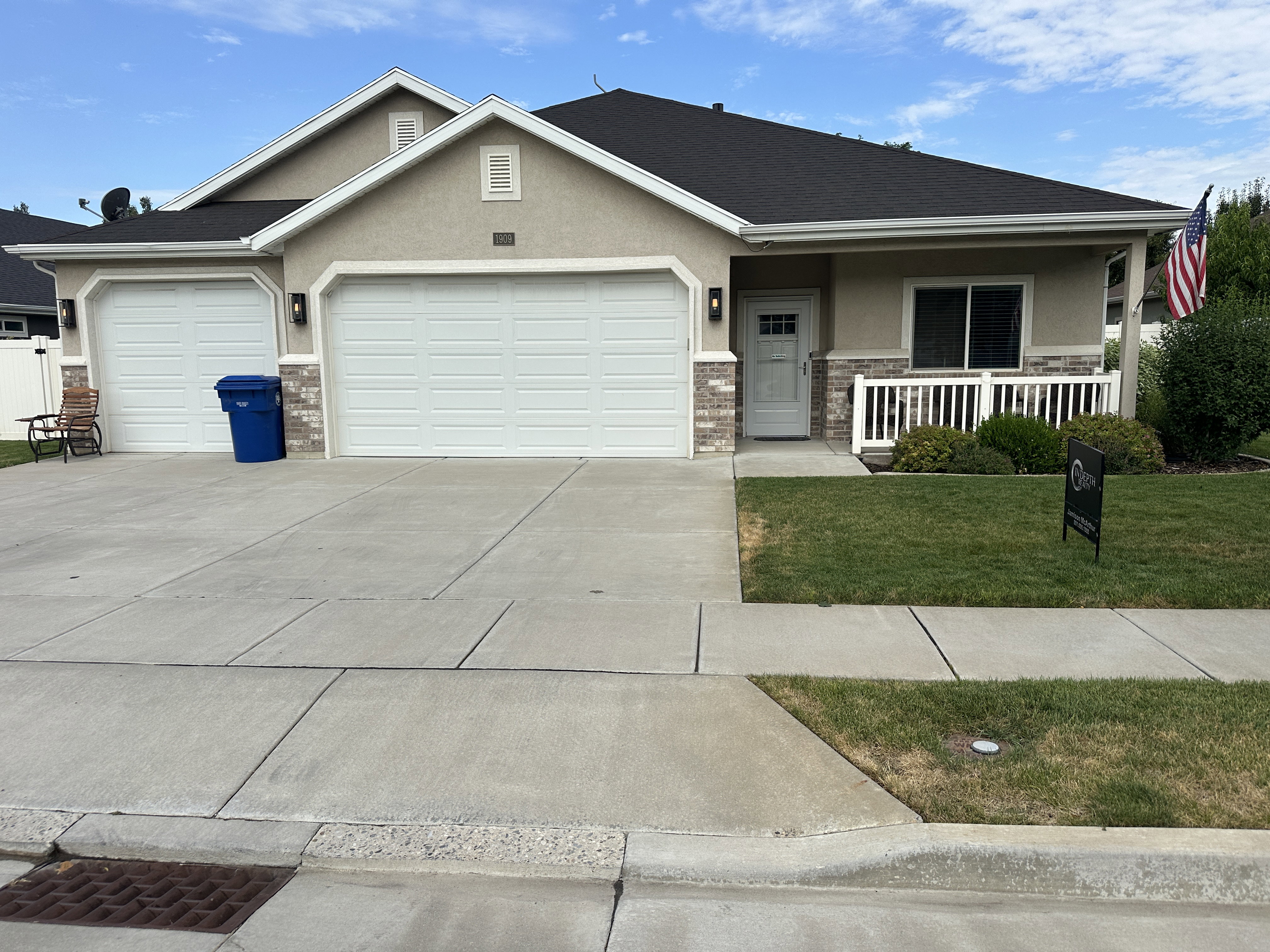 Front exterior featuring a stucco and stone veneer facade, two-car garage, covered porch with white railing, a concrete driveway, and a well-maintained lawn