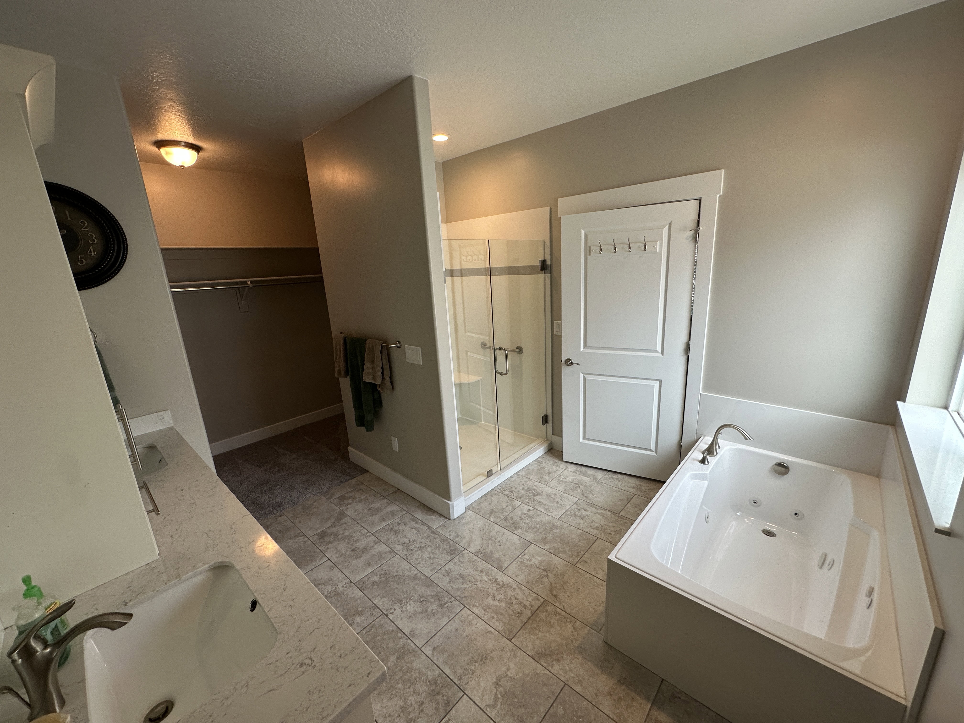 Spacious bathroom featuring a built-in jetted tub, a glass-enclosed shower, dual vanity with undermount sinks, and tile flooring