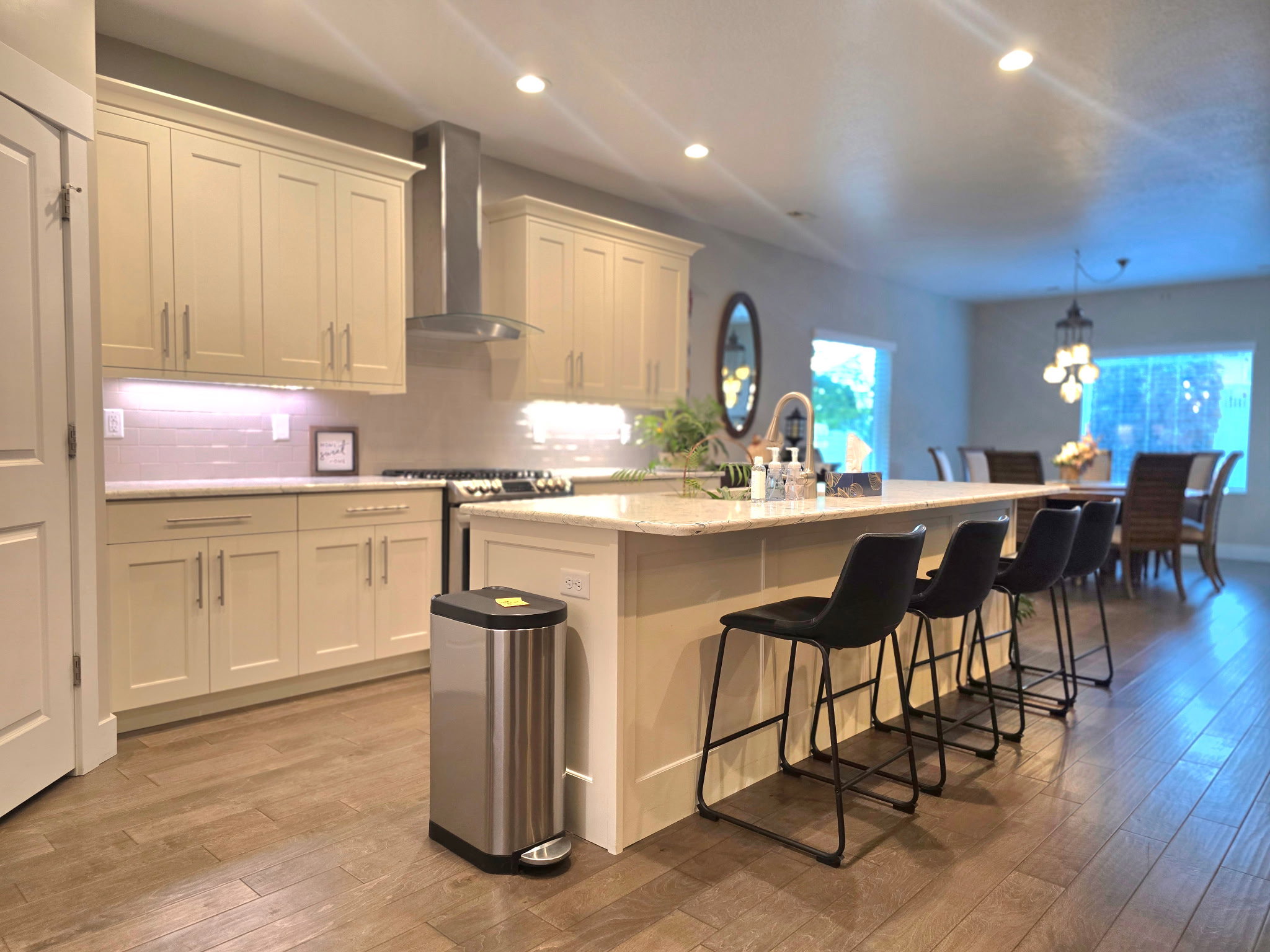 Open-concept kitchen featuring light-toned cabinetry, a stainless steel range hood, and wood-finish flooring