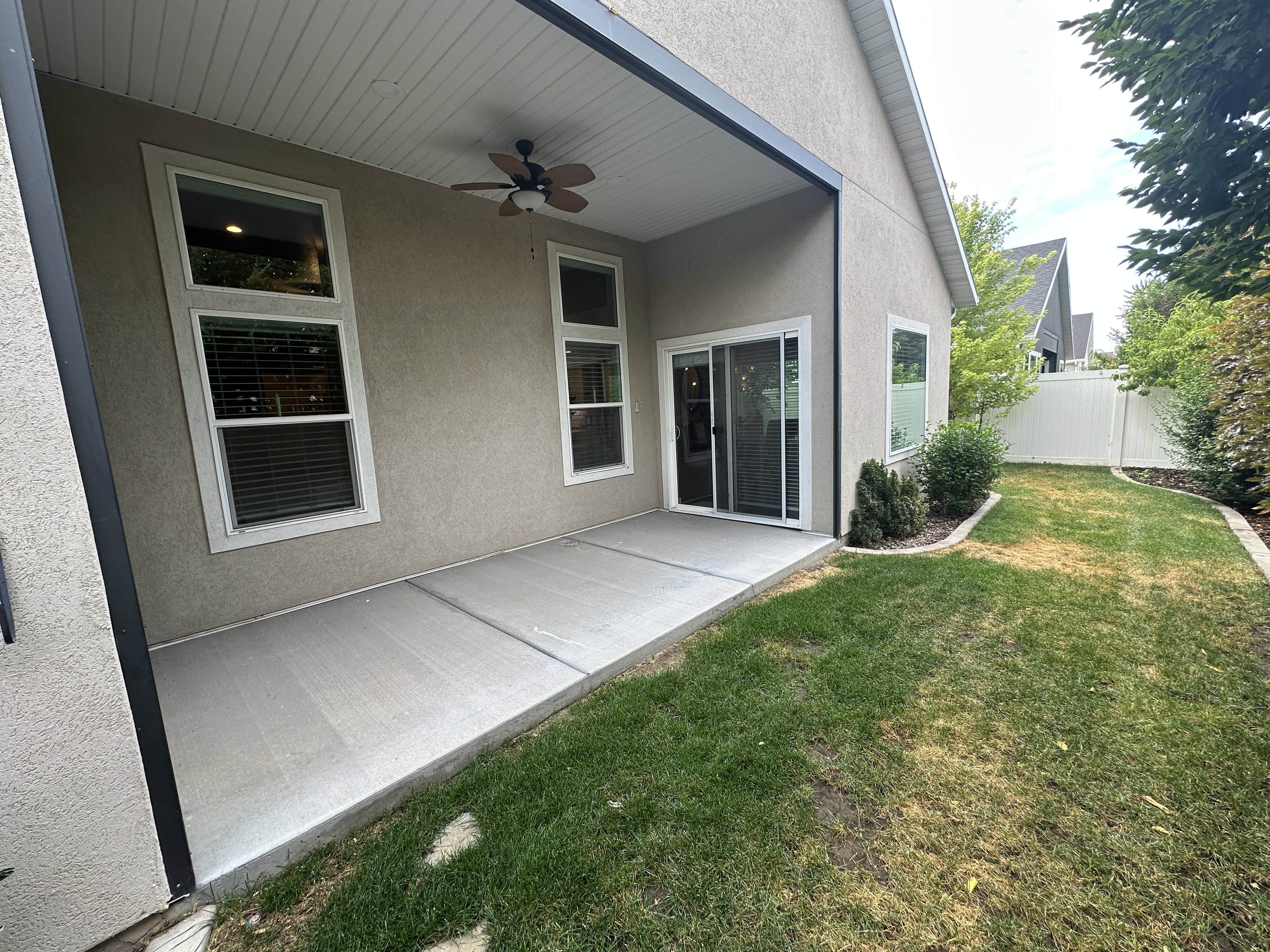 Covered concrete patio featuring an outdoor ceiling fan, multiple windows, and a sliding glass door