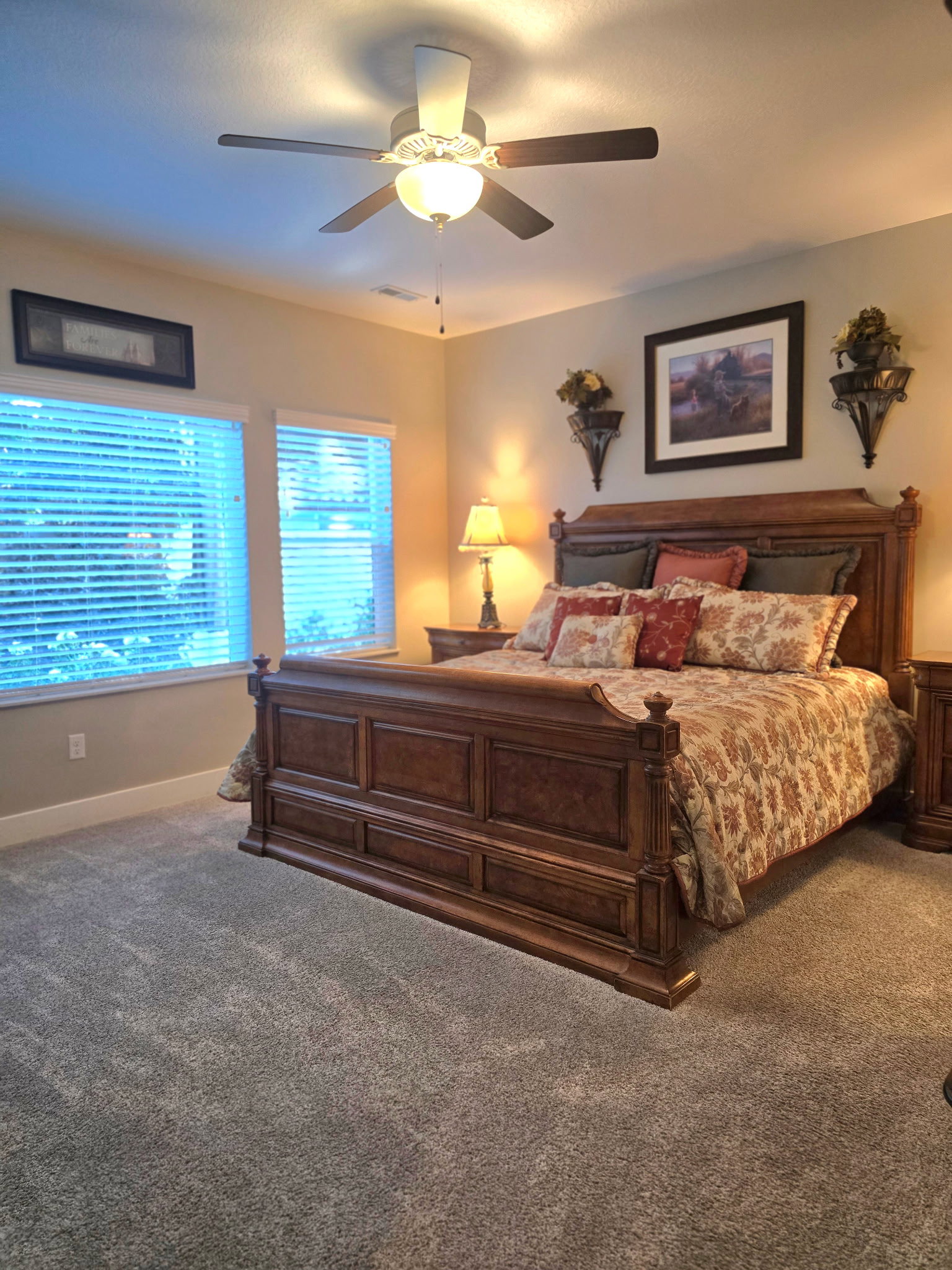 Carpeted bedroom featuring a ceiling fan with integrated lighting, two windows with blinds, and neutral painted walls