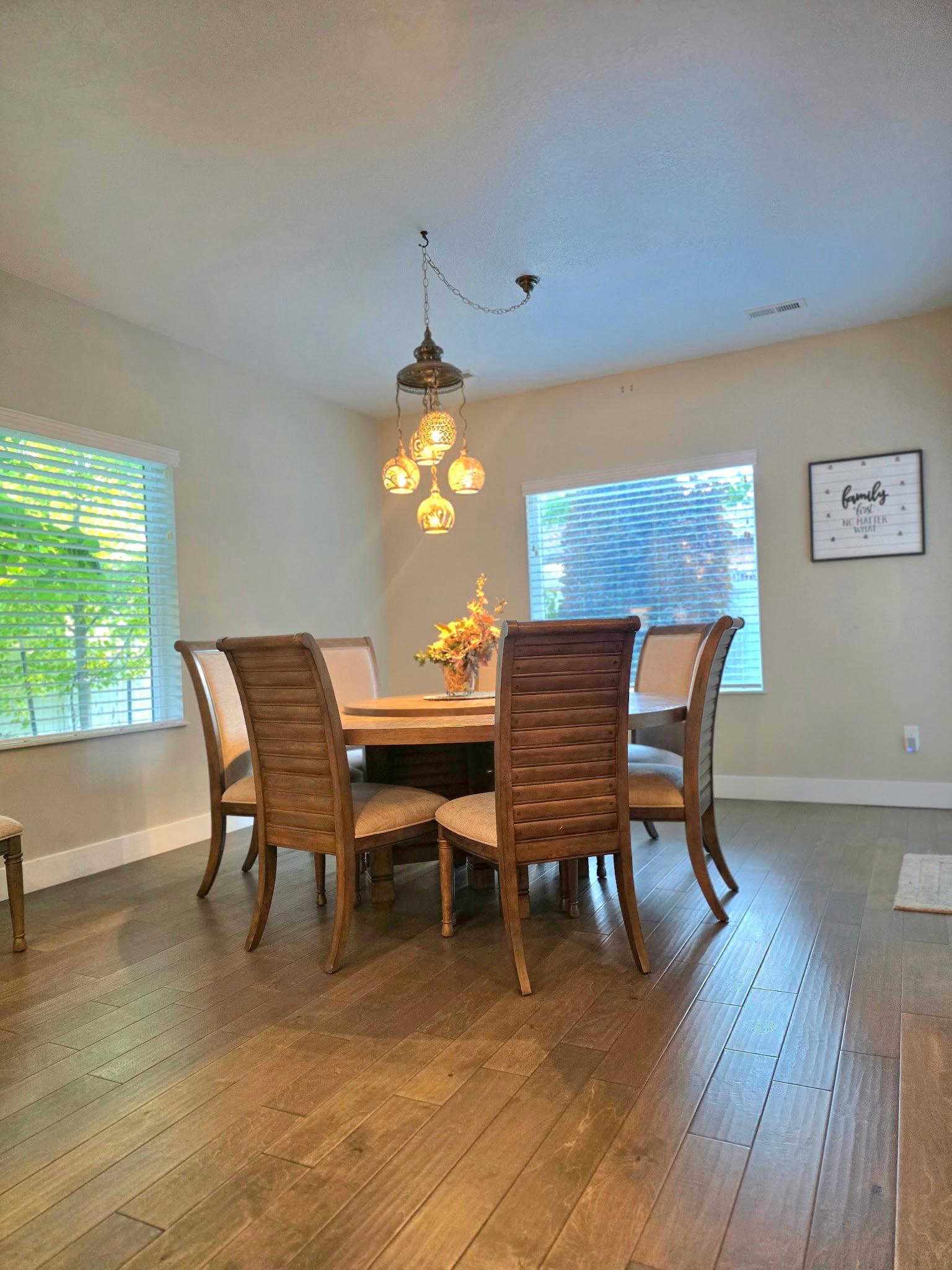Dining area featuring wood-finish flooring, two large windows with horizontal blinds, and a multi-globe pendant light fixture
