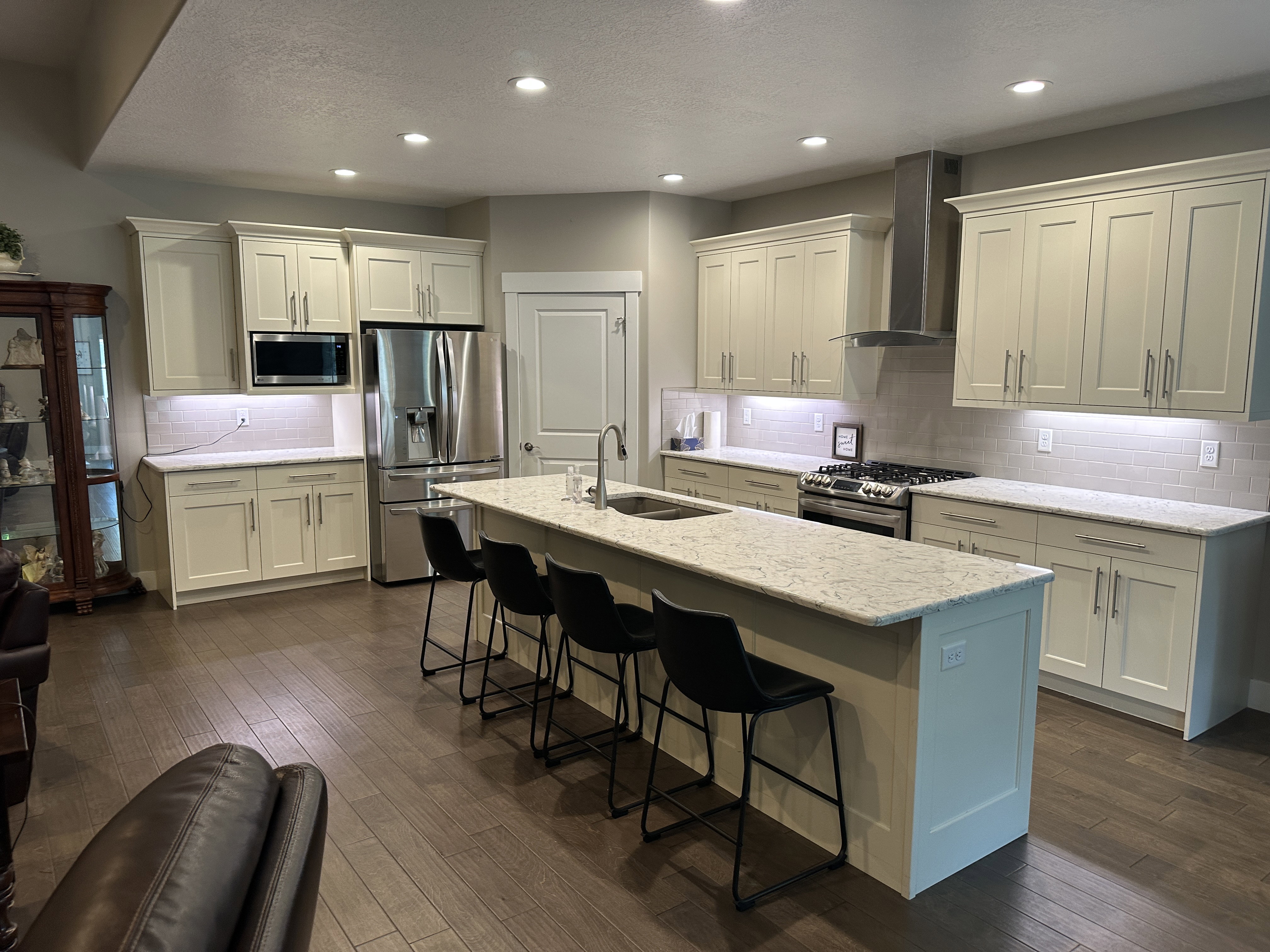 Open-concept kitchen featuring light-toned cabinetry, stainless steel appliances, a center island with seating, stone countertops, and wood-finish flooring