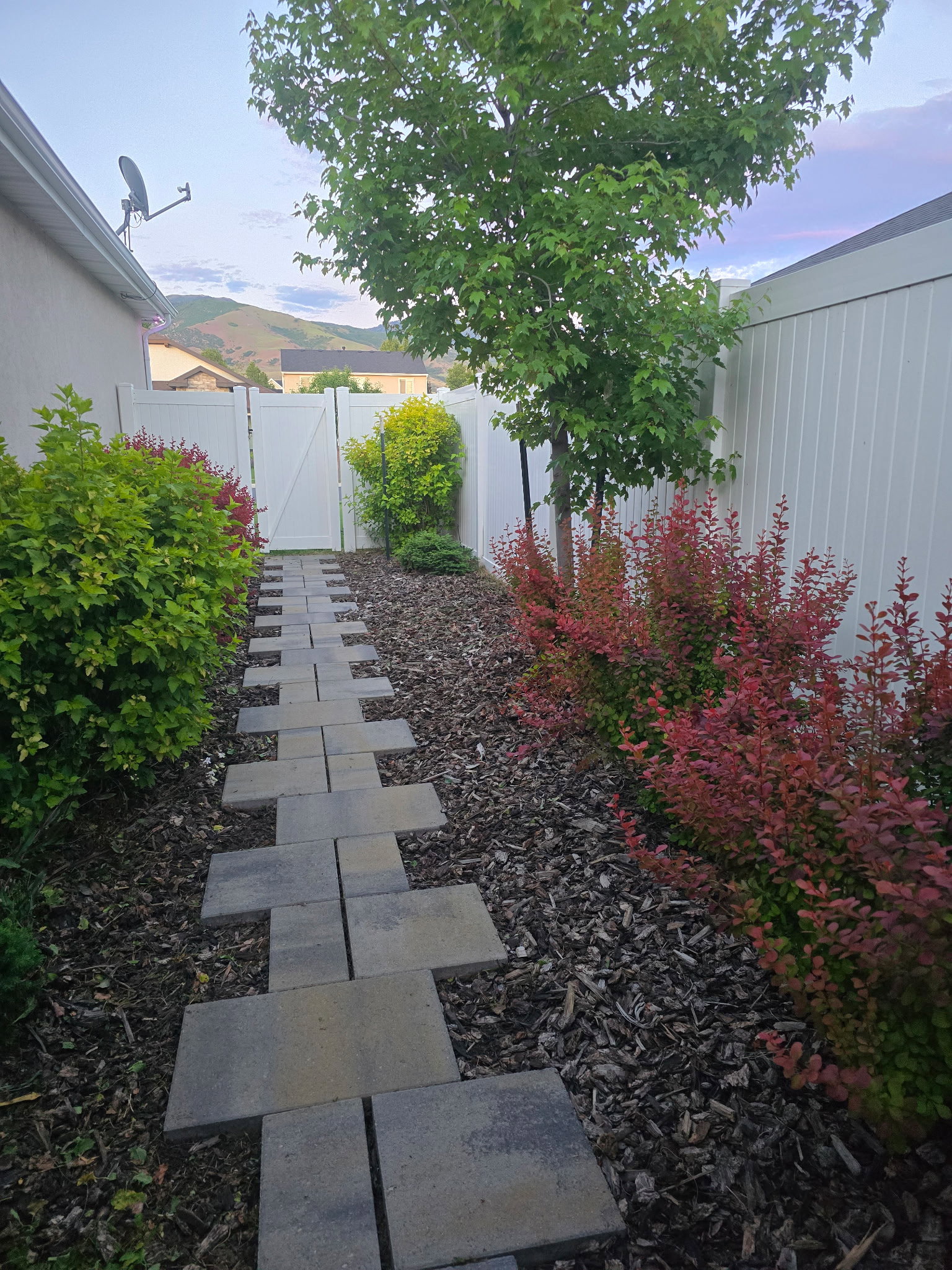 Stepping stone pathway featuring a white vinyl fence and mature shrubbery