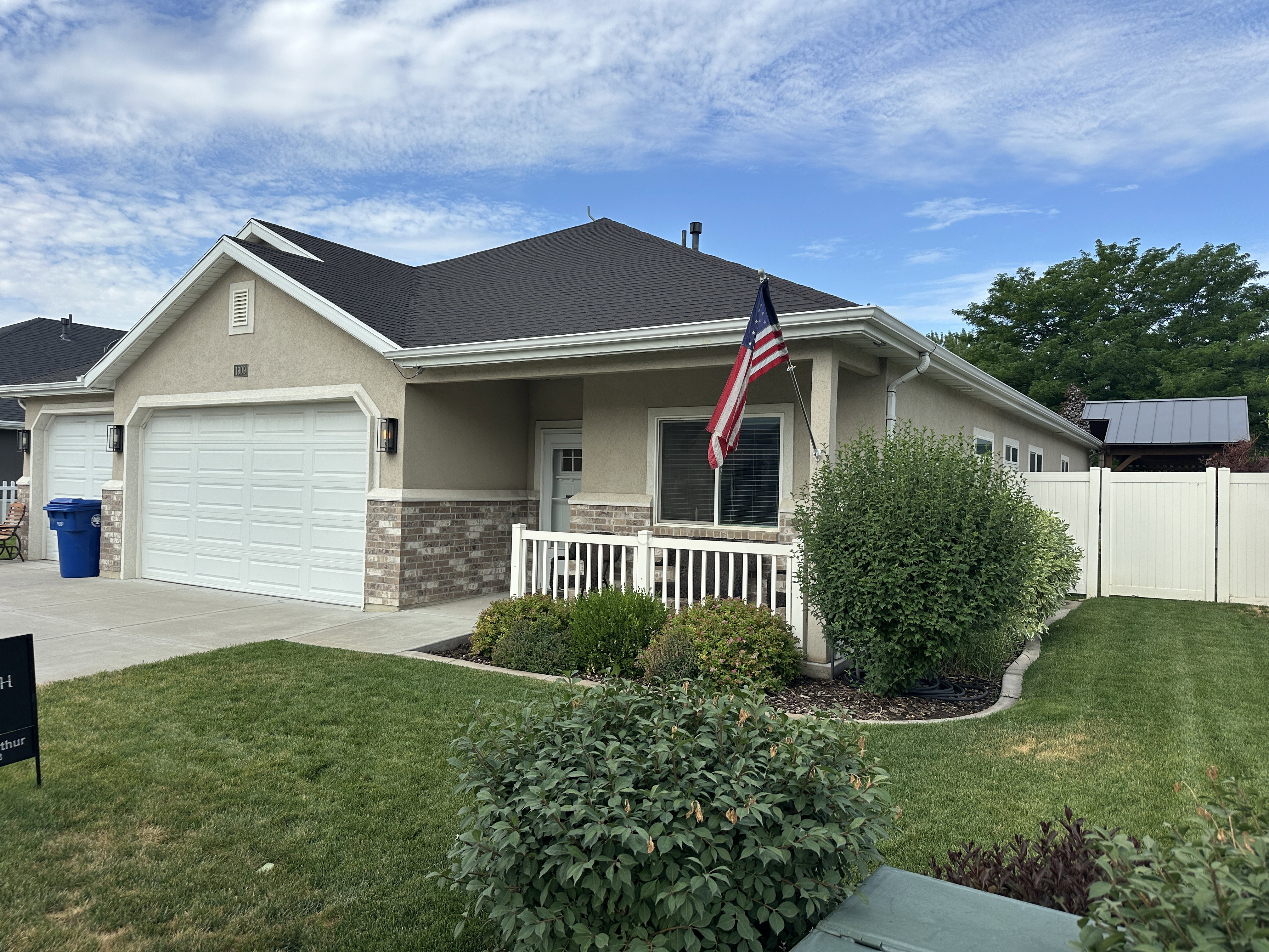 Single-story residence featuring a two-car garage, stucco siding with brick accents, covered front porch, and a white picket fence