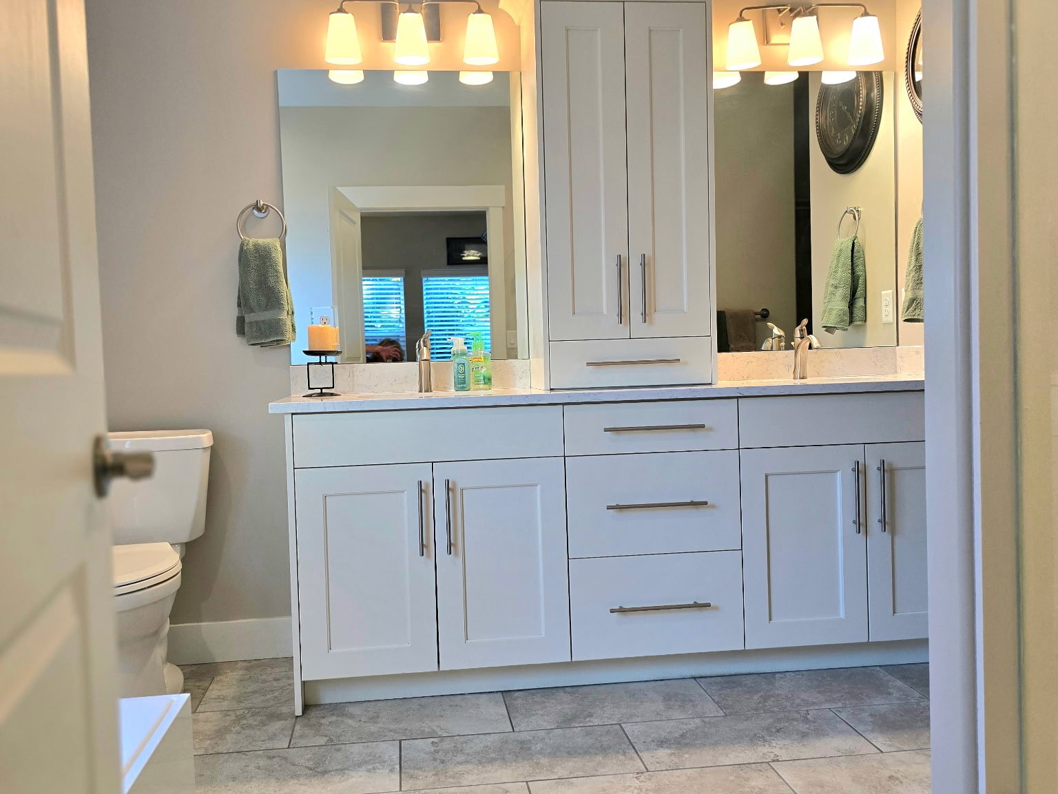 Spacious bathroom featuring light gray tile flooring, a dual vanity with white cabinetry, ample counter space, and a built-in storage tower