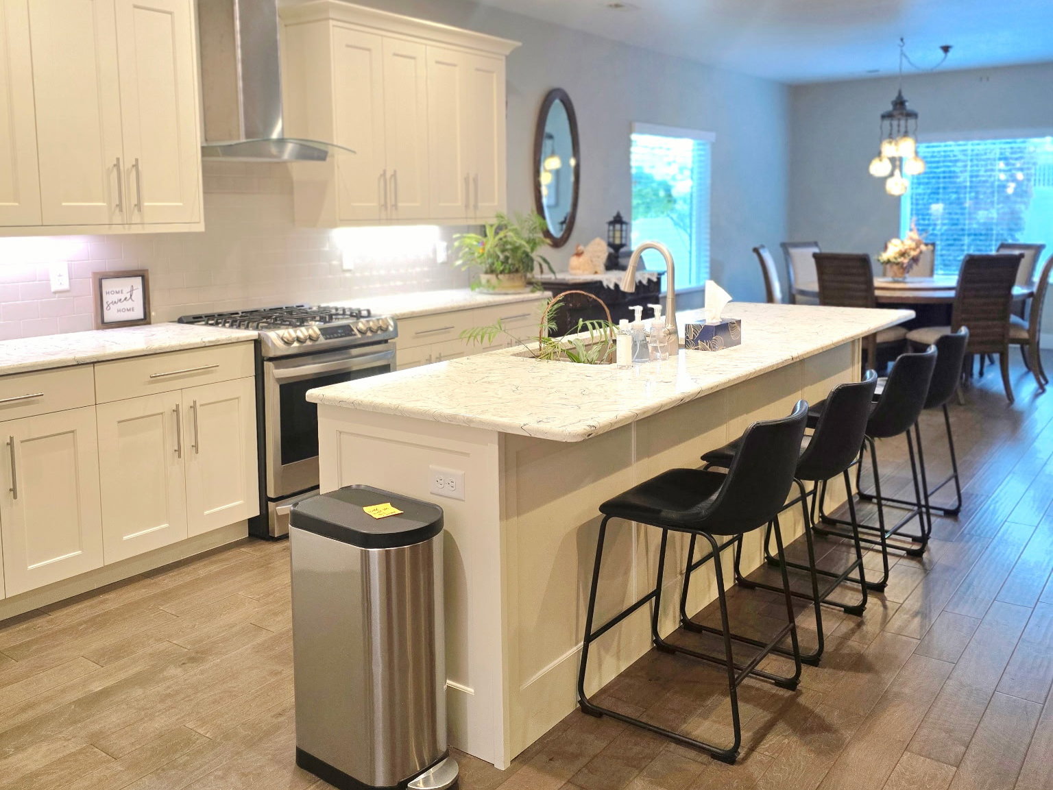 Open-concept kitchen featuring an expansive central island with seating, stainless steel appliances, neutral cabinetry, and wood-finish tile flooring