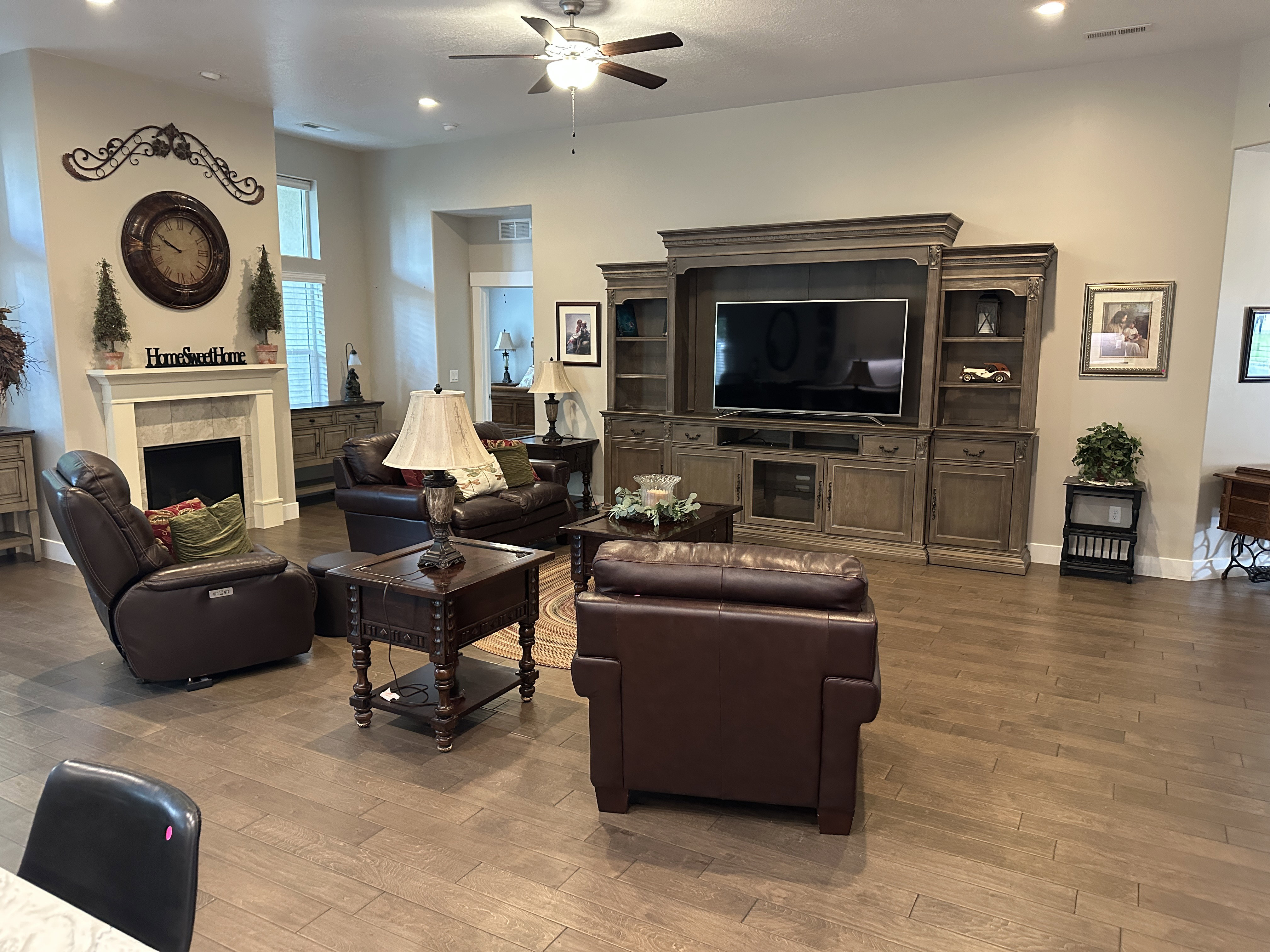 Spacious living area featuring wood-finish flooring, a fireplace with a stone surround and mantle, and a ceiling fan