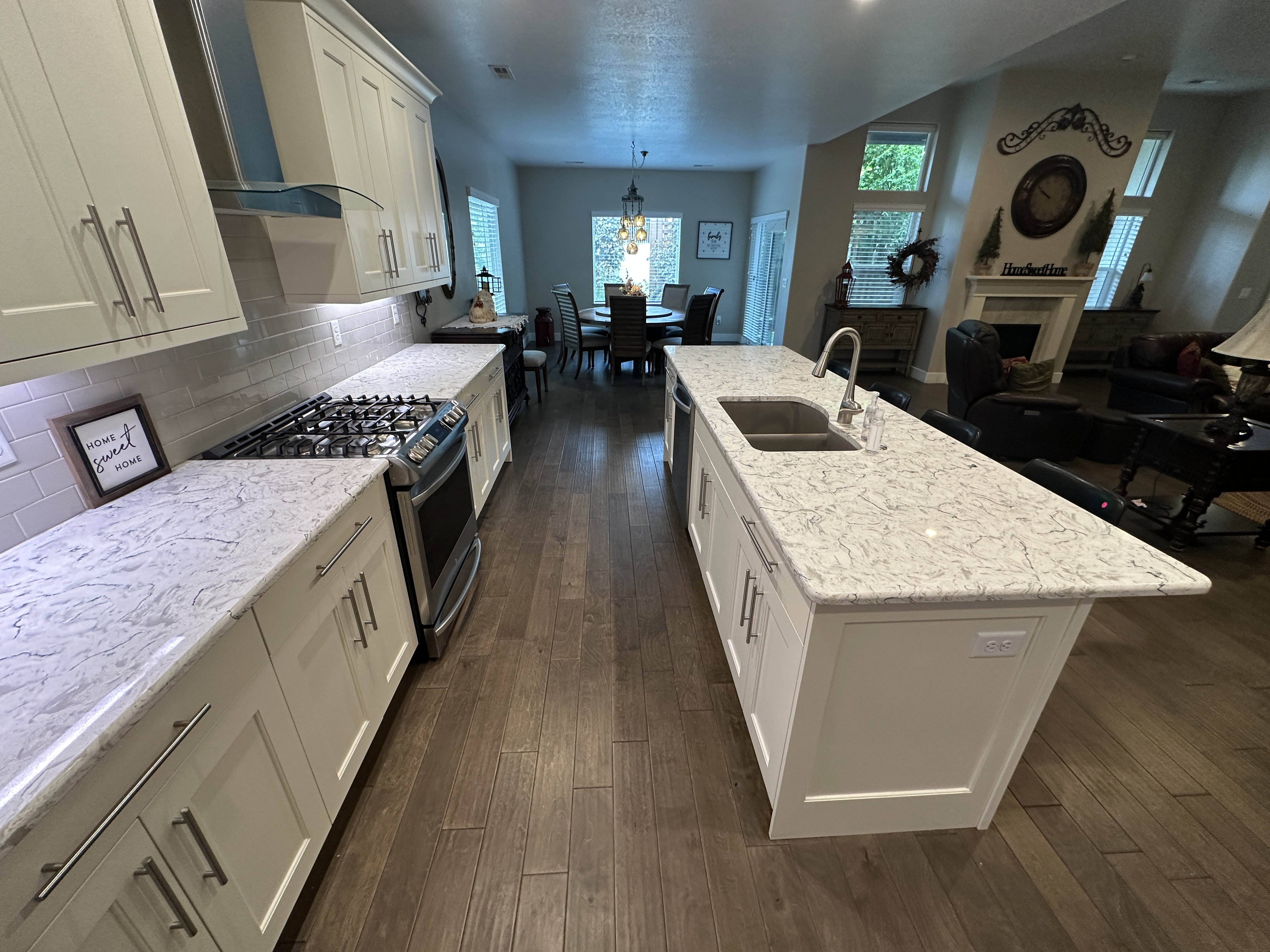 Kitchen featuring white shaker-style cabinetry, light-toned countertops, subway tile backsplash, a gas range with a stainless steel vent hood, and wood-finish flooring throughout