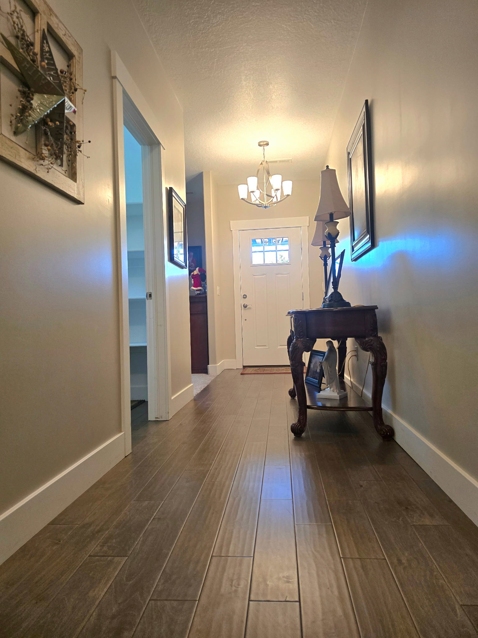 Bright hallway featuring wood-finish flooring, a white paneled entry door with frosted glass inserts, and a multi-arm chandelier
