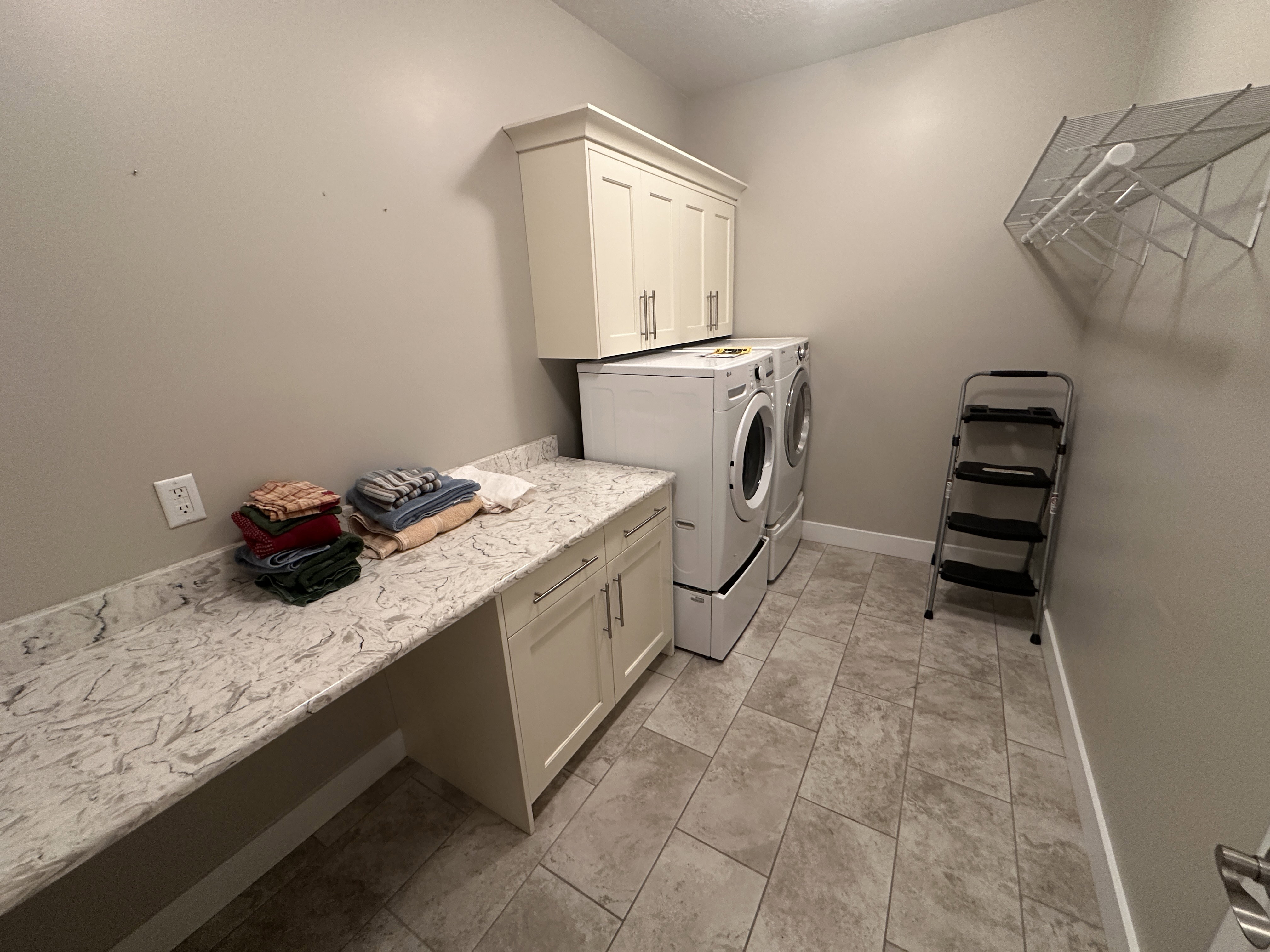 Laundry room featuring extensive stone-look countertops, custom cabinetry, ceramic tile flooring, and neutral wall tones