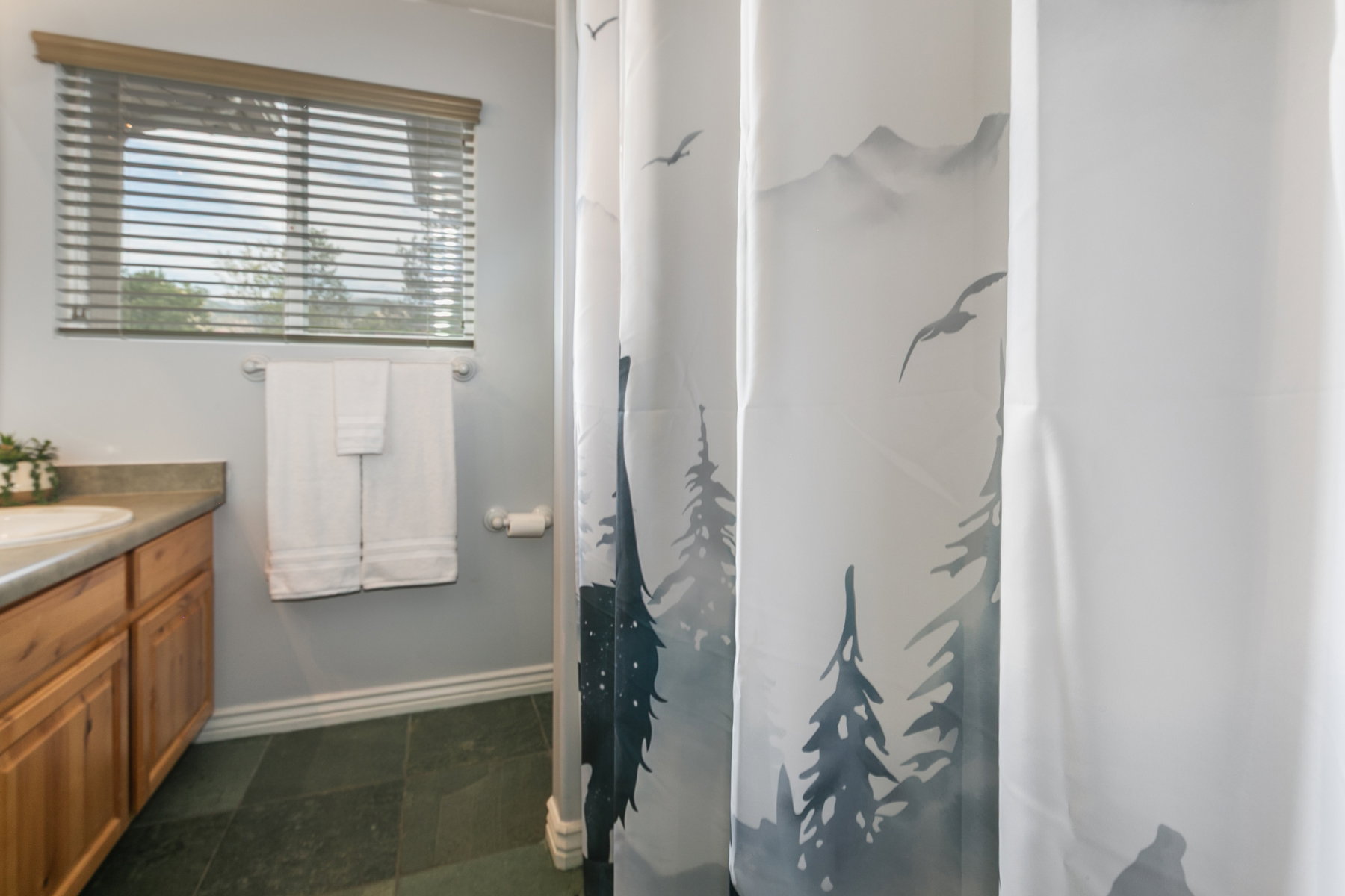 Bathroom featuring a window with blinds, wood-finish vanity with an integrated sink, and dark tile flooring