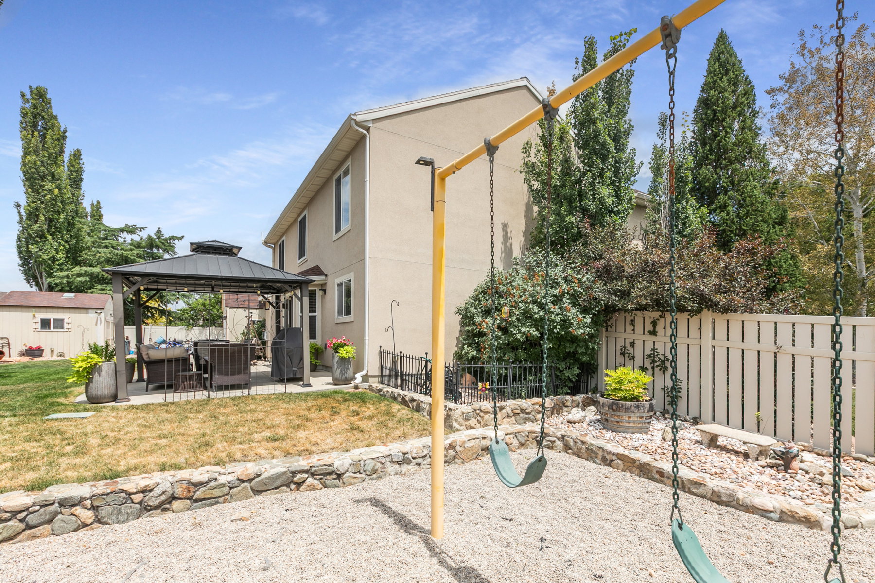 Backyard featuring a gravel play area with a swing set, a stone retaining wall, and a patio with a gazebo