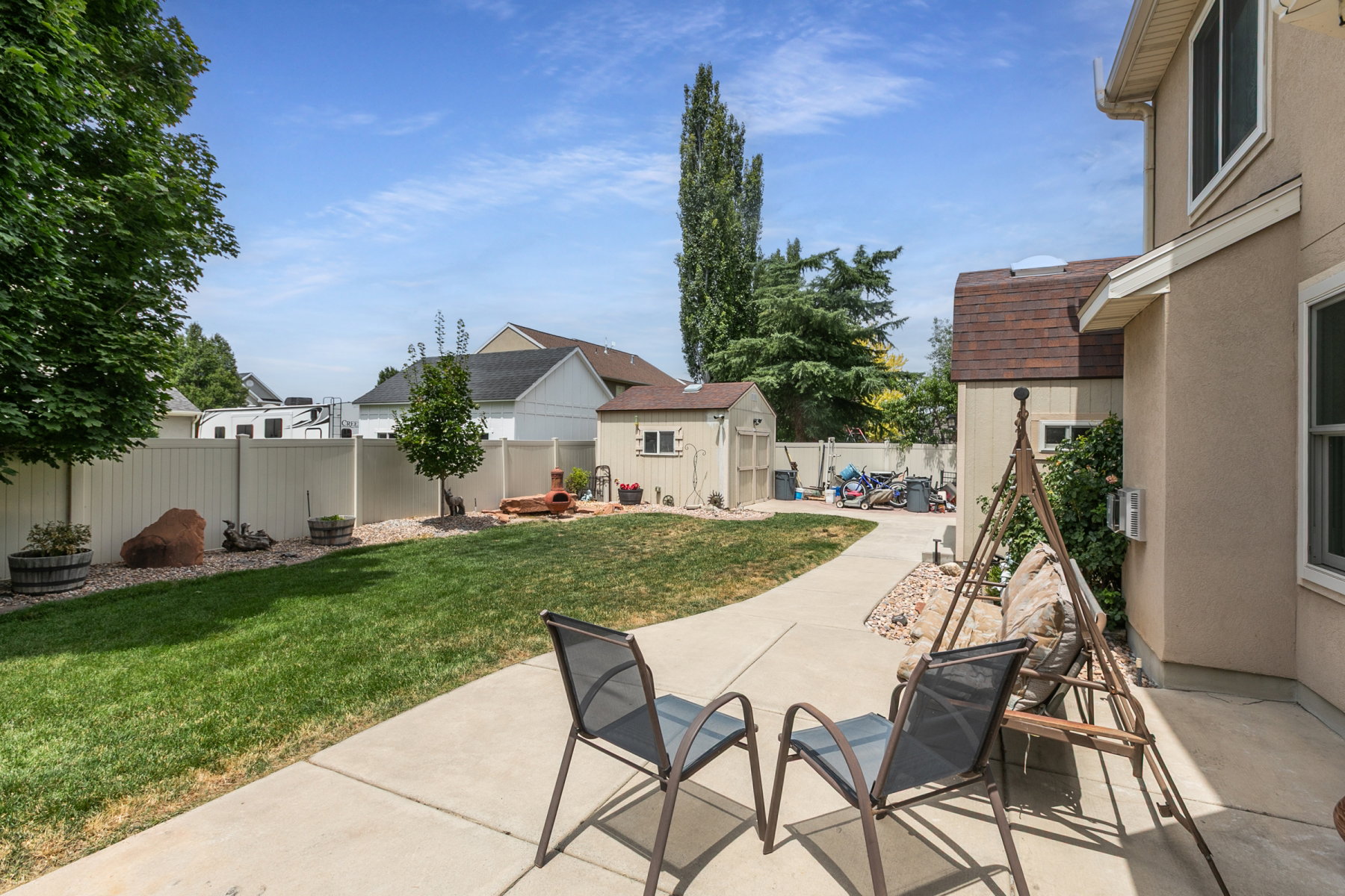 Expansive backyard featuring a concrete patio, a manicured lawn, a concrete pathway, a storage shed, and a privacy fence