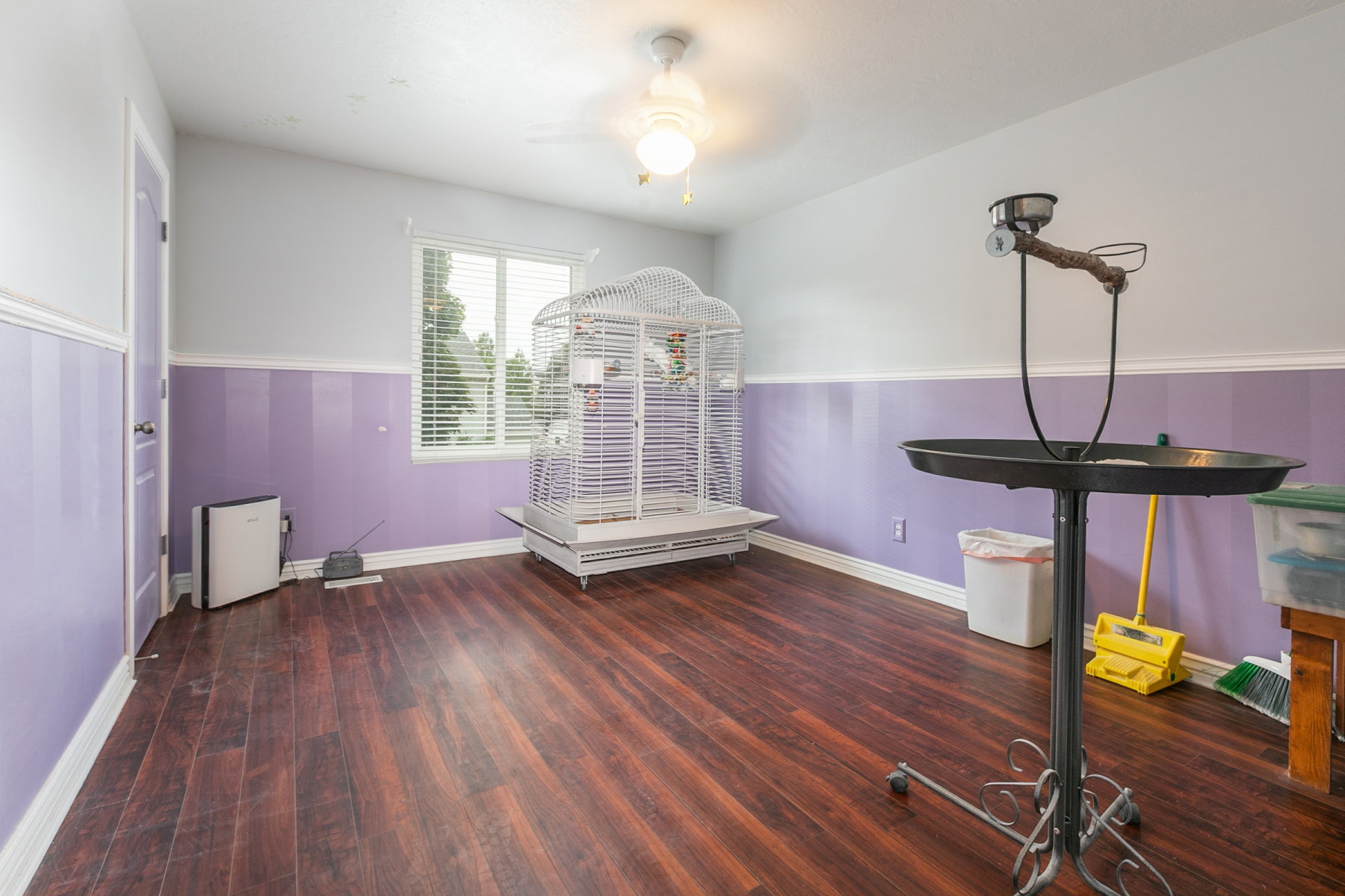 Spacious room featuring rich wood-finish flooring, a window with blinds, and a ceiling fan