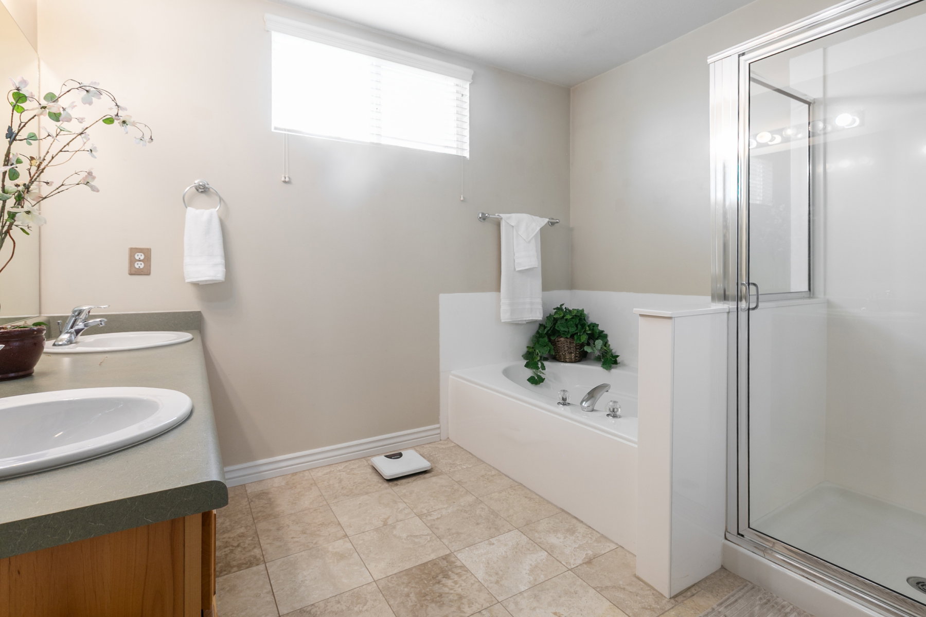 Primary bathroom featuring a built-in jetted tub, a glass-enclosed shower, and a dual-sink vanity with a solid surface countertop