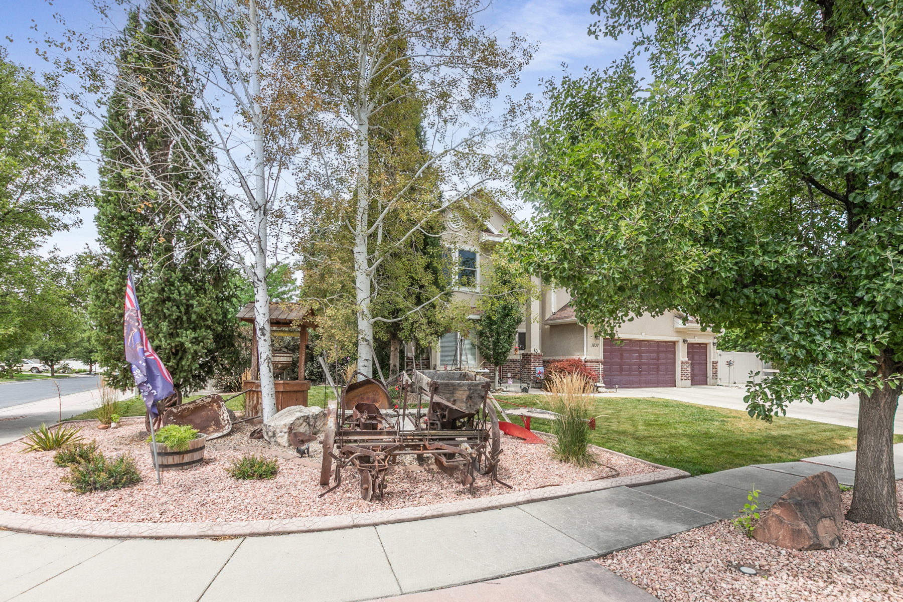 Landscaped front yard featuring mature trees, decorative gravel, wishing-well, and a concrete pathway