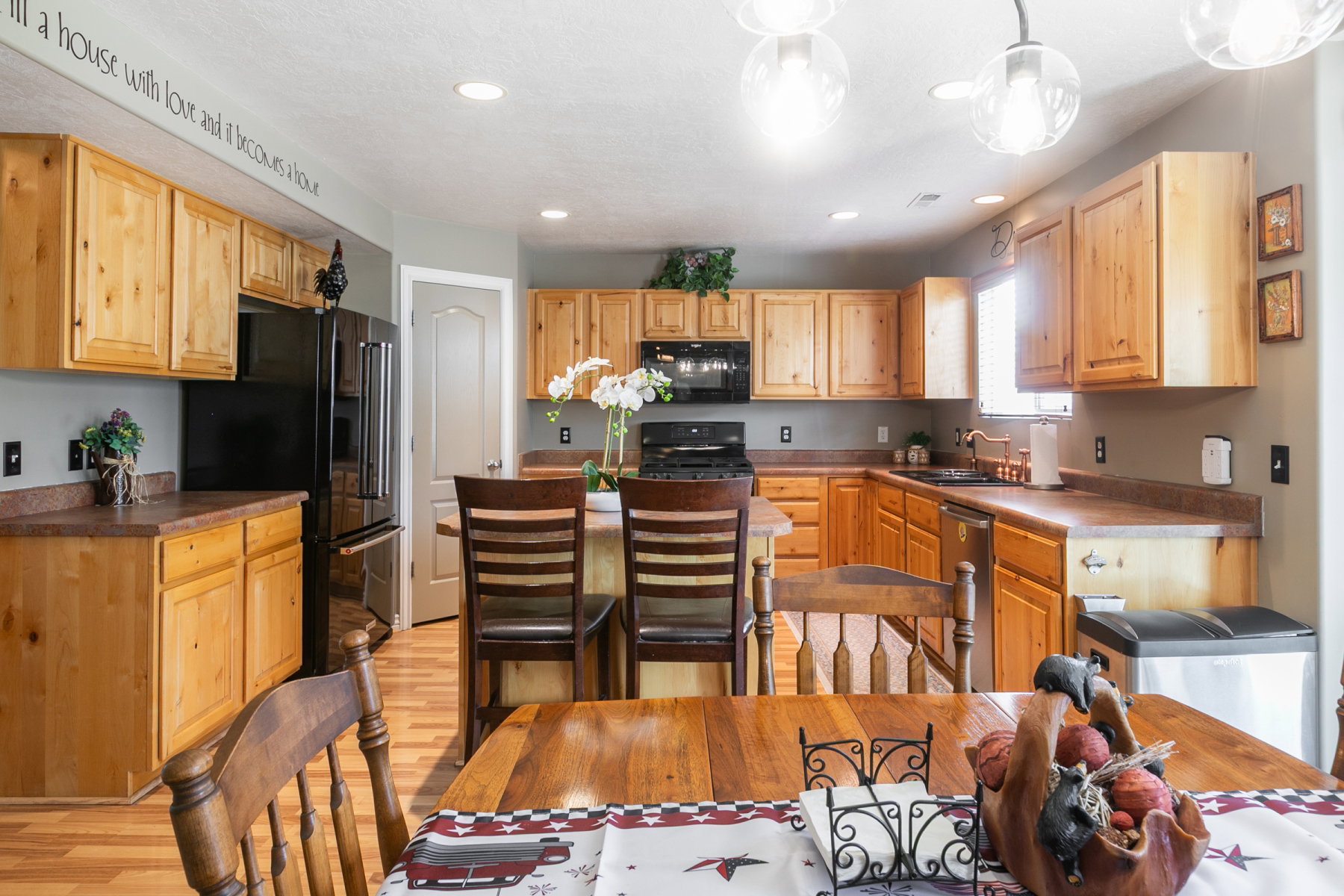 Kitchen featuring light wood-finish cabinetry, dark countertop surfaces, black appliances, and recessed lighting