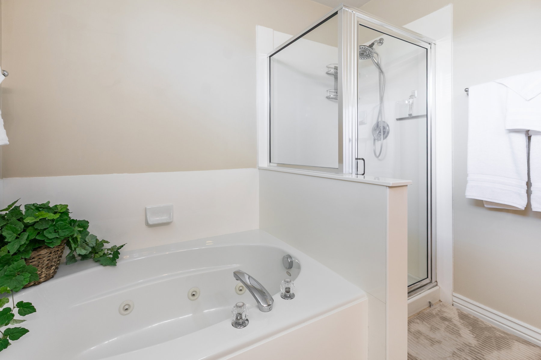 Jetted tub with chrome fixtures, glass-enclosed shower with a handheld showerhead, and tiled flooring