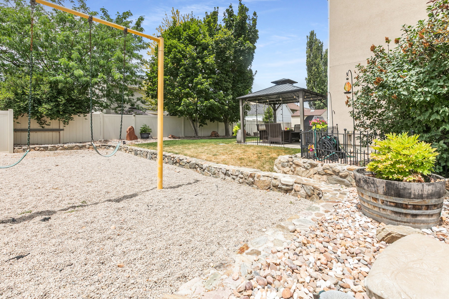 Spacious backyard featuring a dedicated play area with ground cover, a rock-lined garden bed, a stone hardscaped pathway, a metal gazebo, and a privacy fence