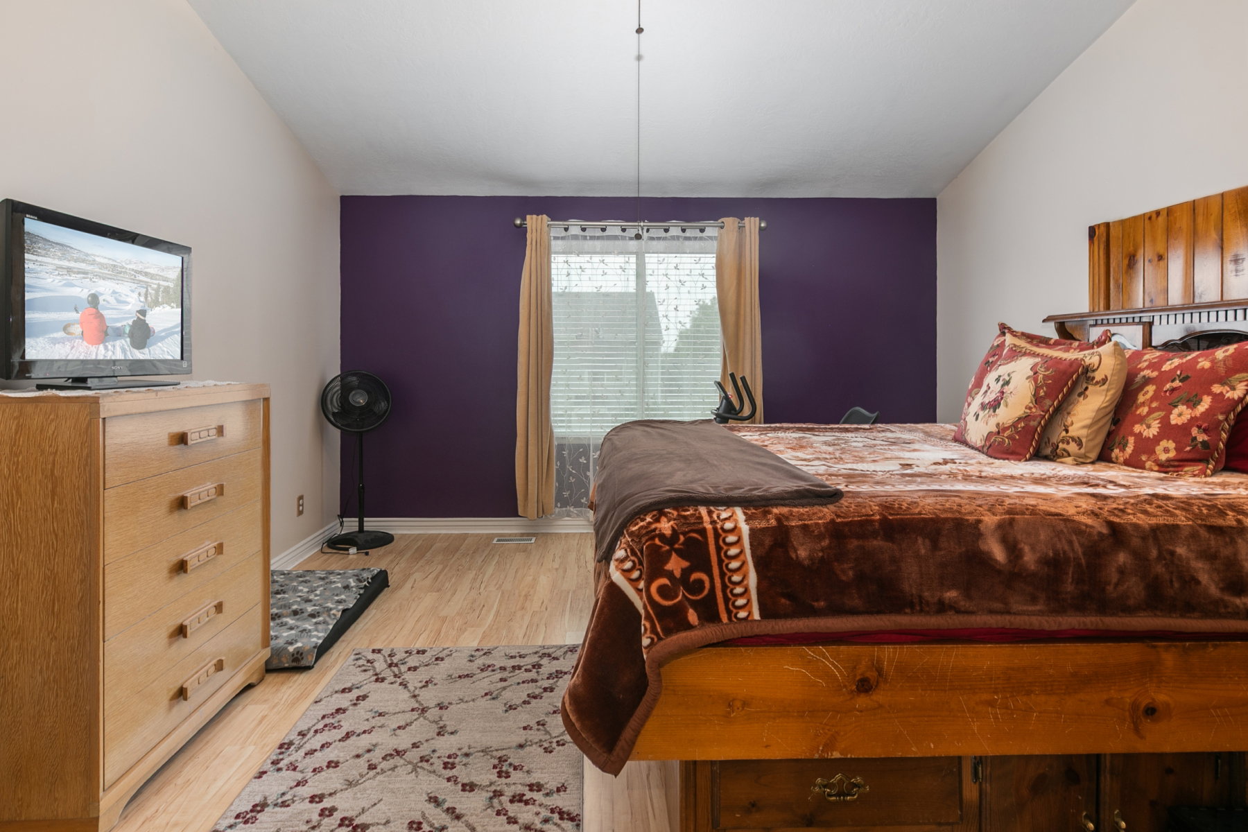 Spacious primary room featuring wood-finish flooring, a window with blinds, and a distinctive accent wall