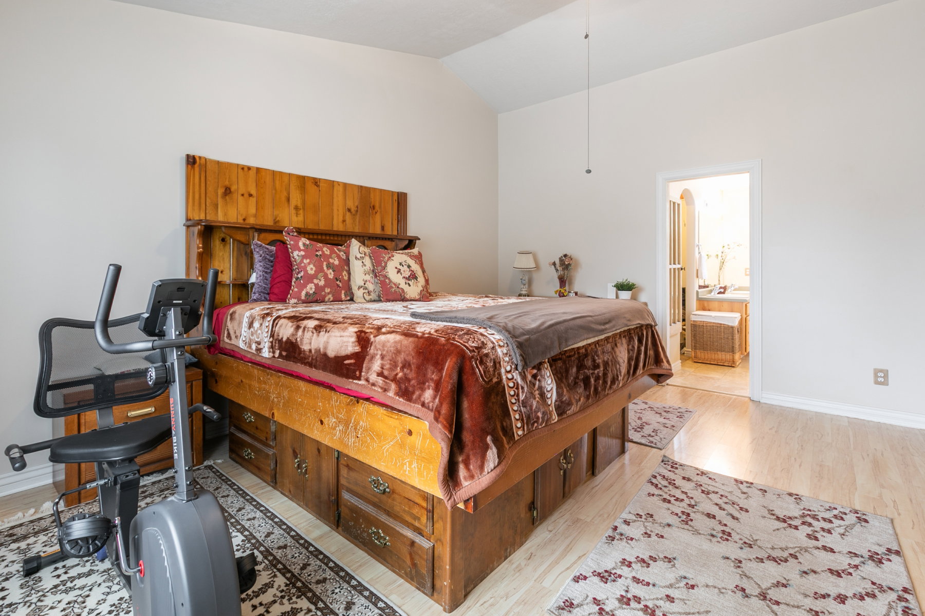 Primary bedroom featuring vaulted ceiling, wood-finish flooring, and an open doorway to an adjoining room