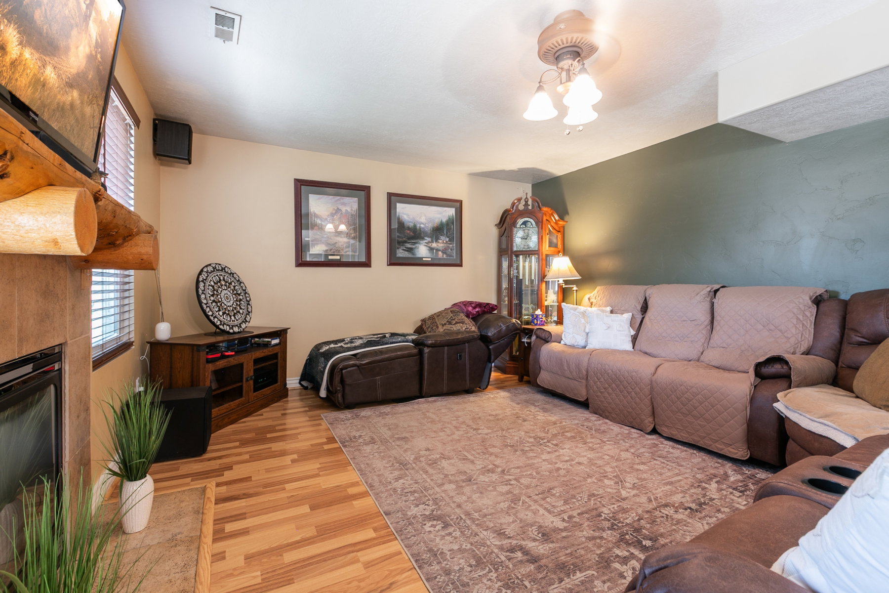 Spacious living area featuring wood-finish flooring, a fireplace with a log mantel and tile surround, and a ceiling fan