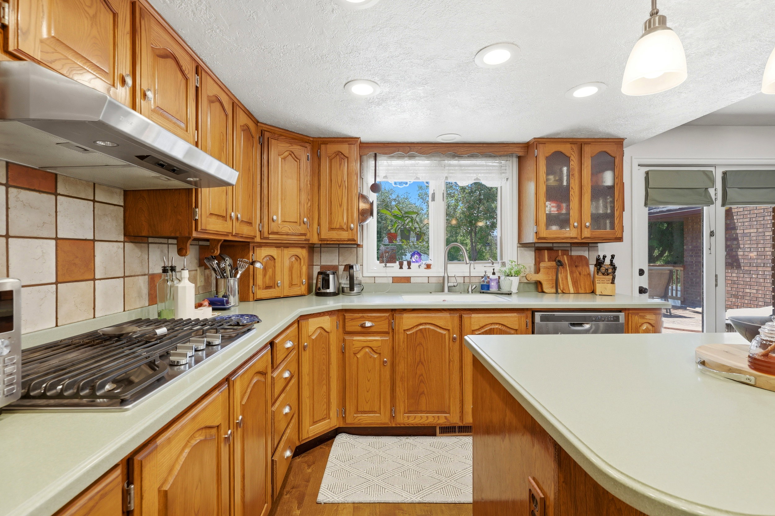 Kitchen featuring wood cabinetry, light-toned countertops, tile backsplash, and stainless steel appliances