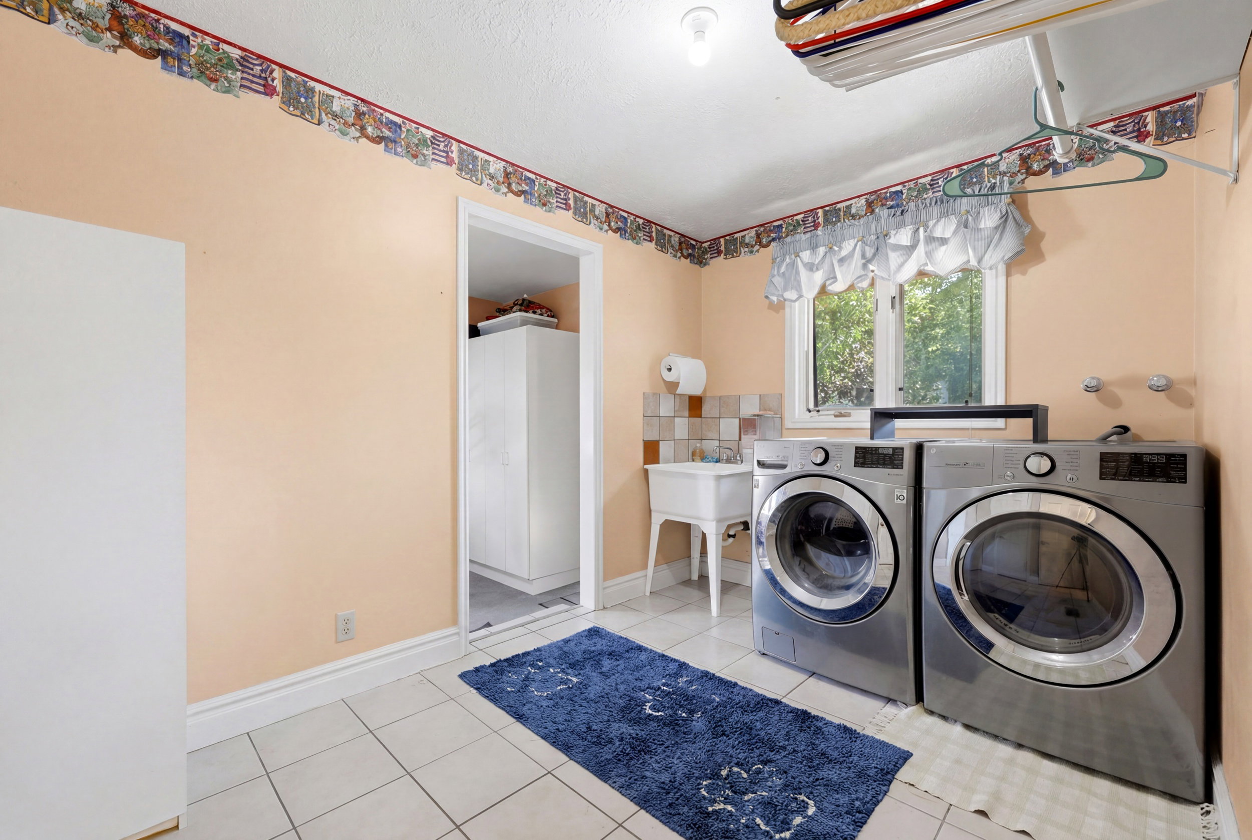 Utility room featuring tiled flooring, a double window, and an attached laundry sink with tiled backsplash