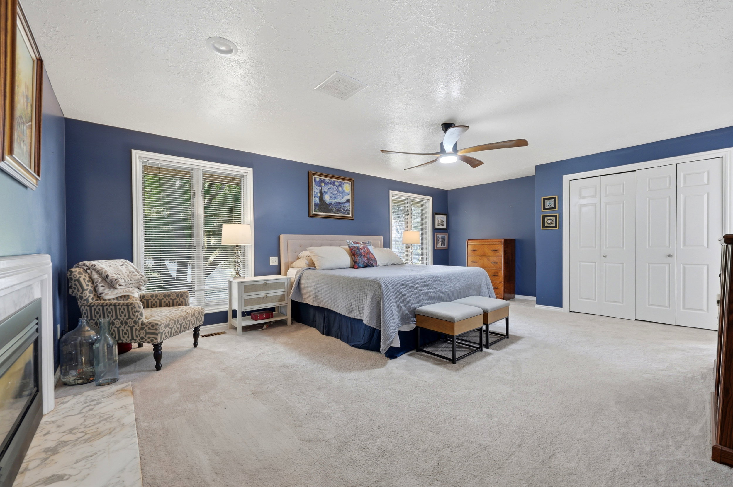 Spacious room featuring light-colored carpeting, multiple windows with blinds, and white bi-fold closet doors