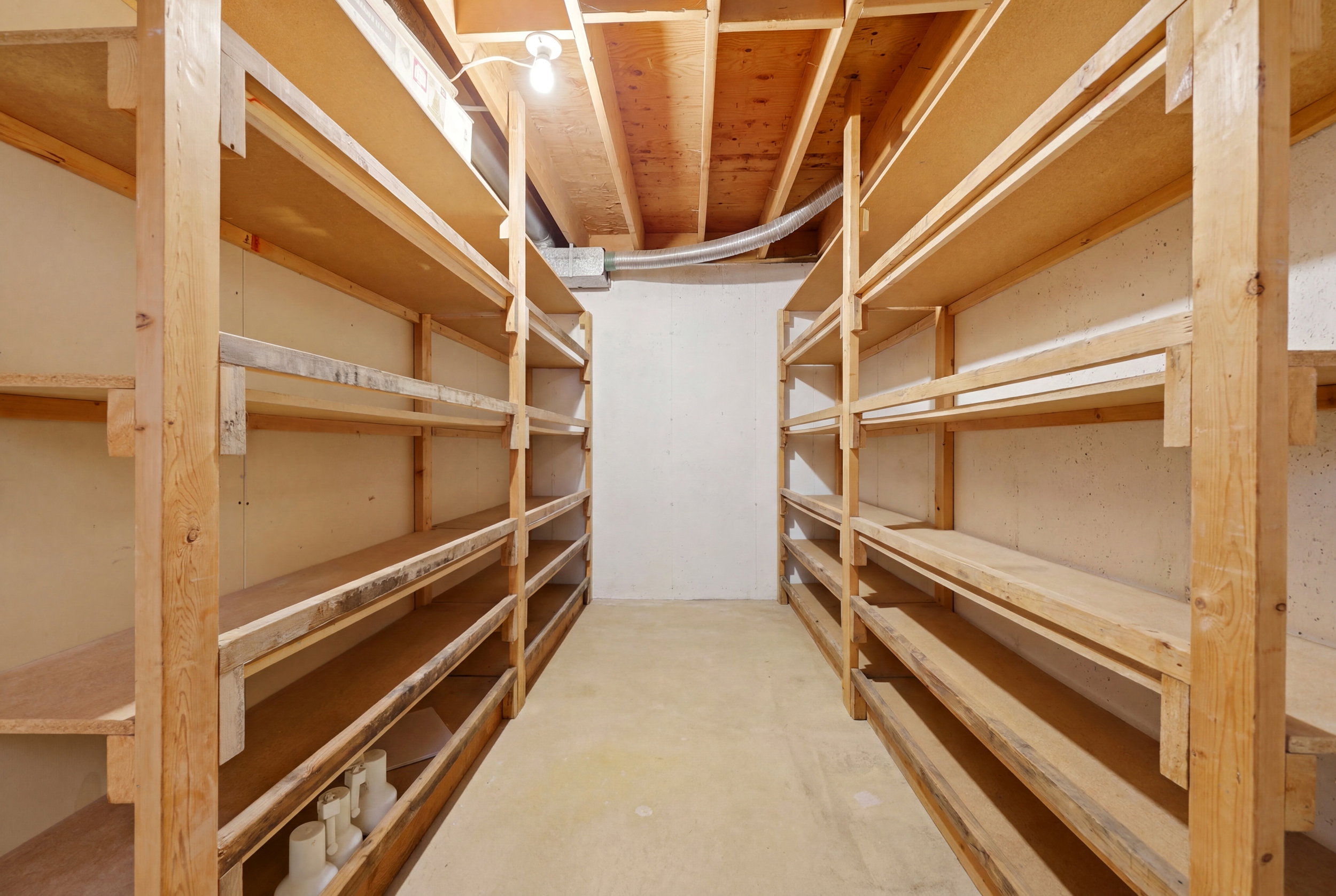 Basement storage area featuring extensive built-in wooden shelving on concrete walls