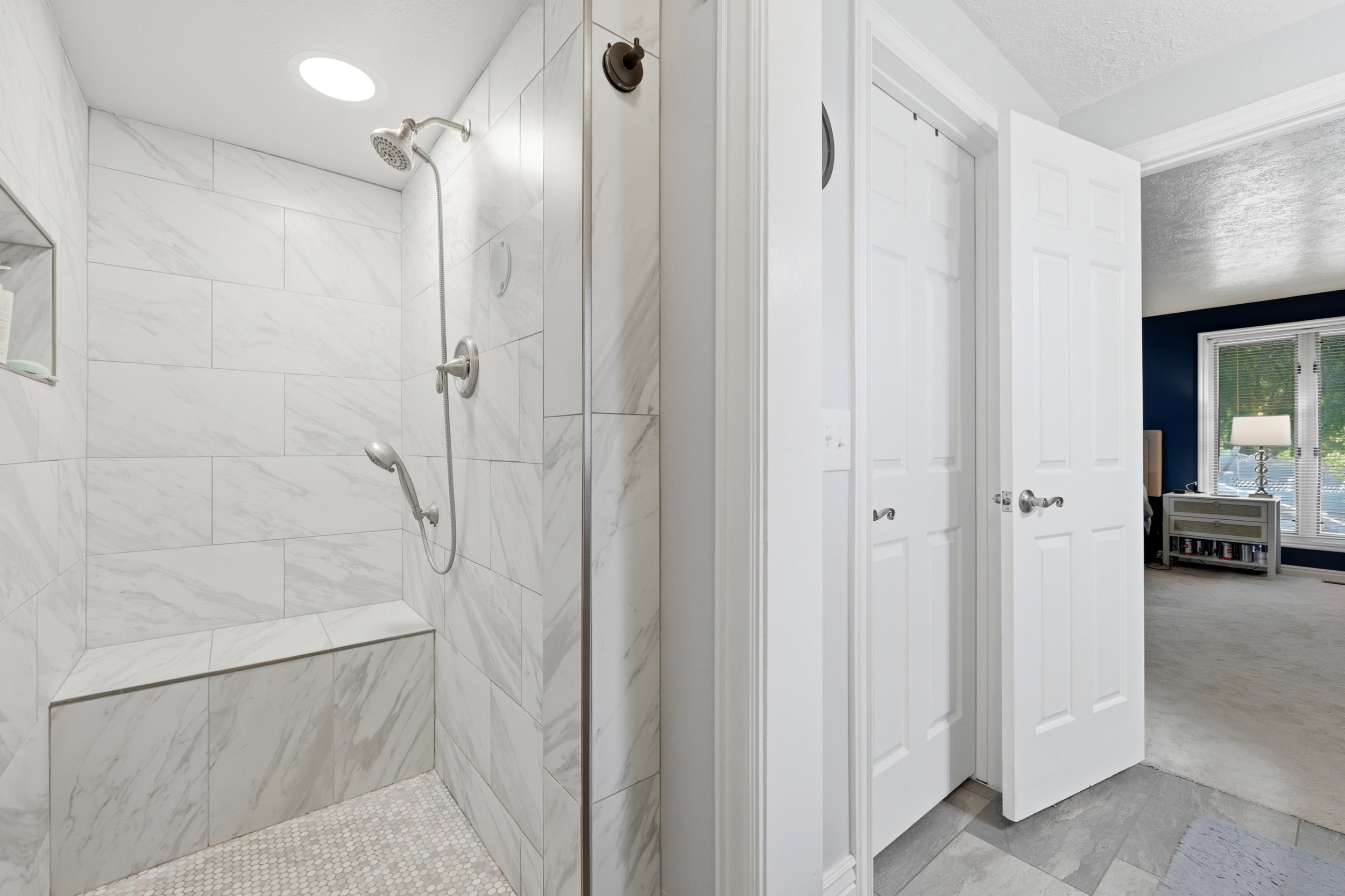 Walk-in shower featuring large format wall tiling, a built-in bench, and a recessed niche