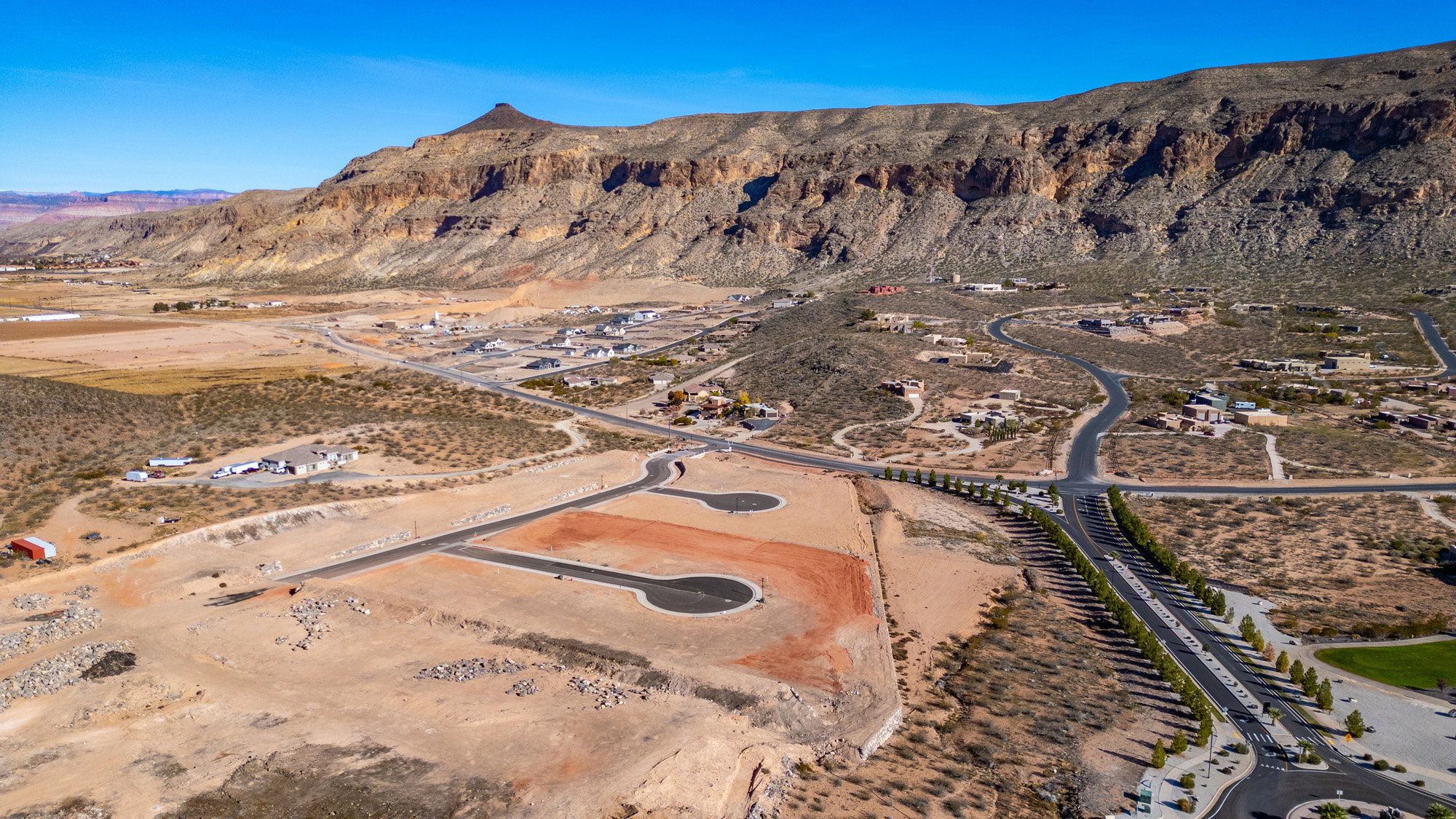 Expansive land parcel featuring prepared building pads and paved roads, surrounded by desert landscaping