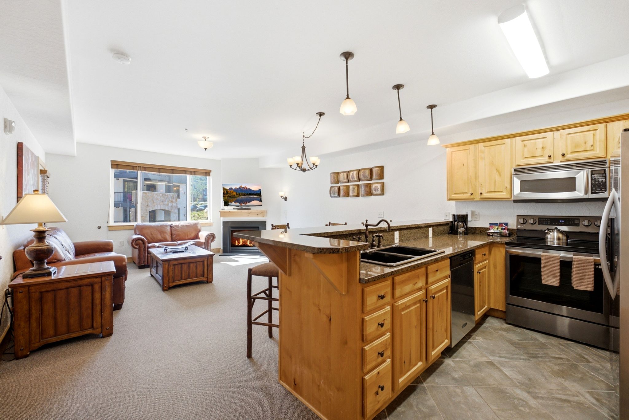 Open-concept living area featuring a kitchen island with seating, a built-in fireplace, stainless steel appliances, and a window with exterior architectural elements