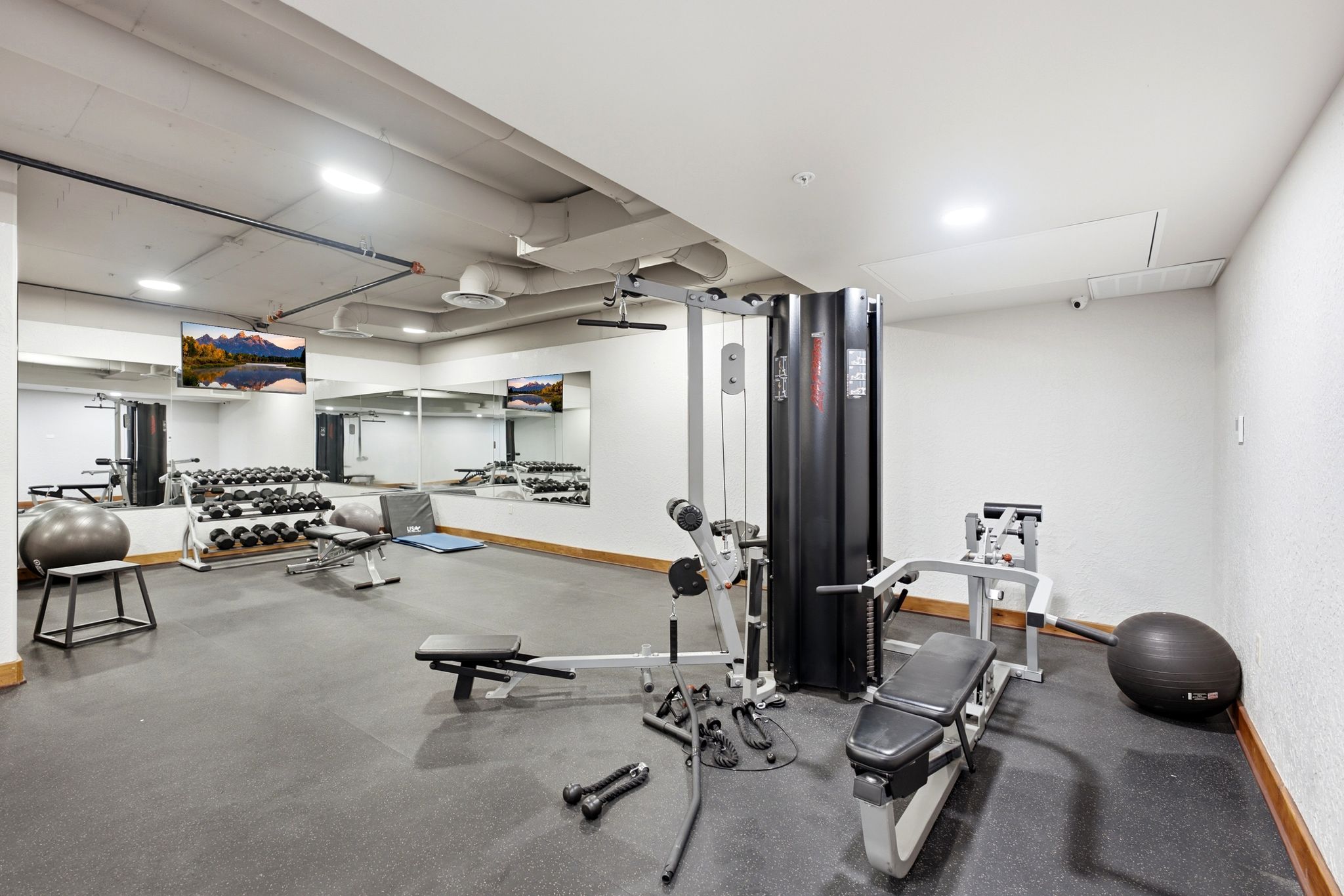 Fitness center featuring dark rubber flooring, mirrored walls, recessed lighting, and wall-mounted televisions