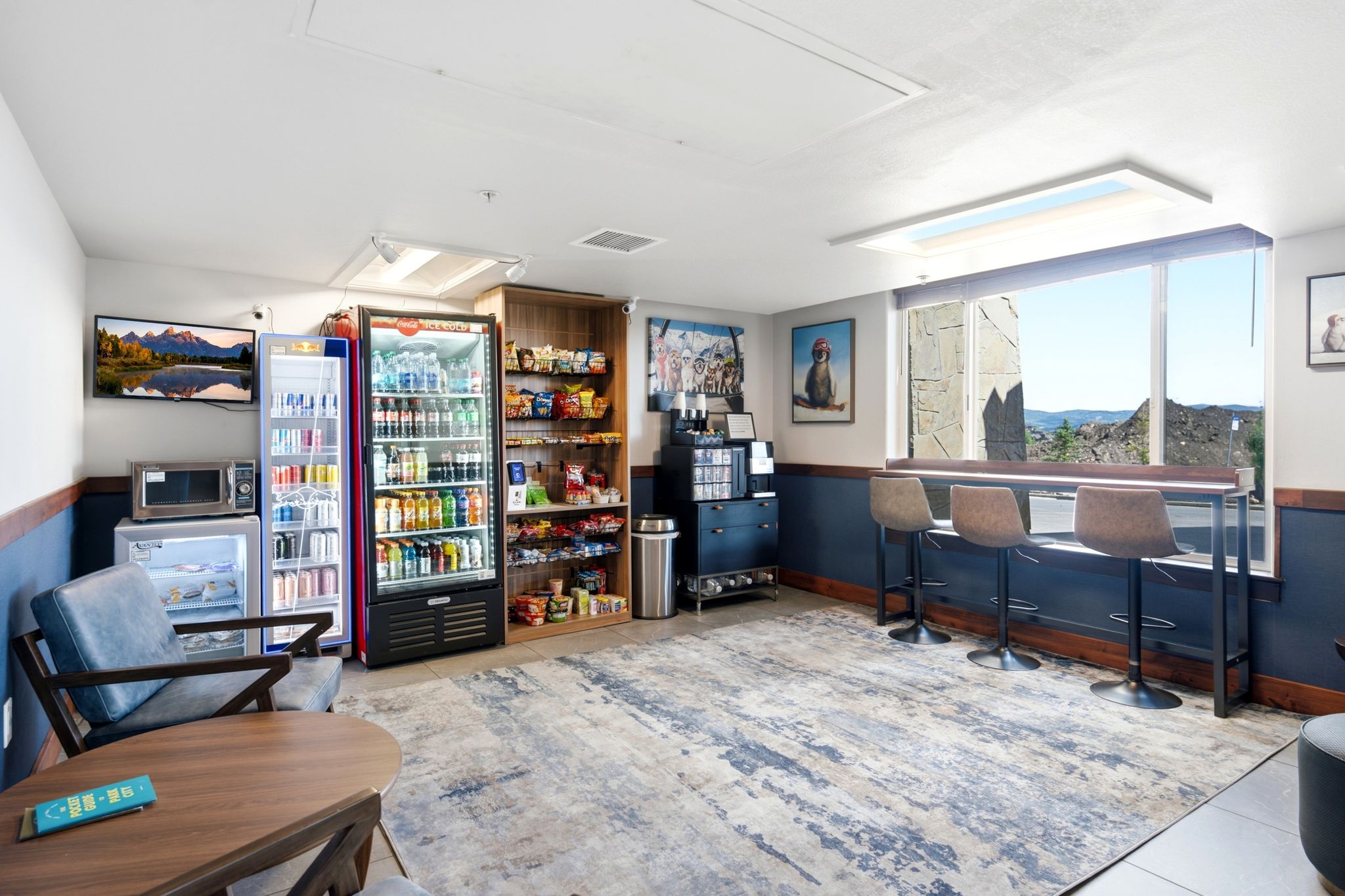 Spacious common area featuring large picture windows, a built-in counter-height bar with seating, a selection of commercial beverage coolers, and a wall-mounted television