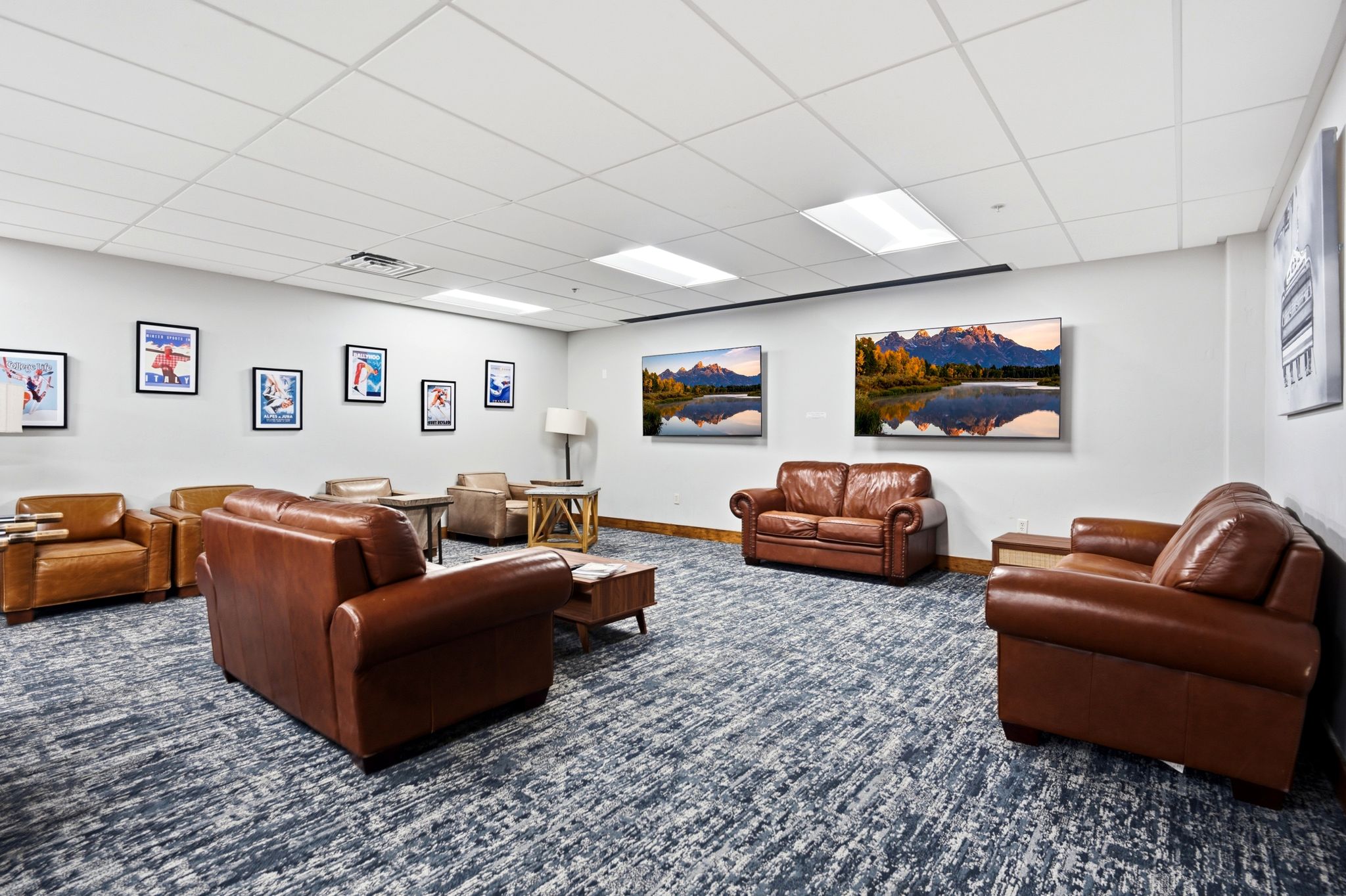 Spacious common area featuring textured blue-grey carpeting, white walls, and a white grid ceiling with recessed lighting
