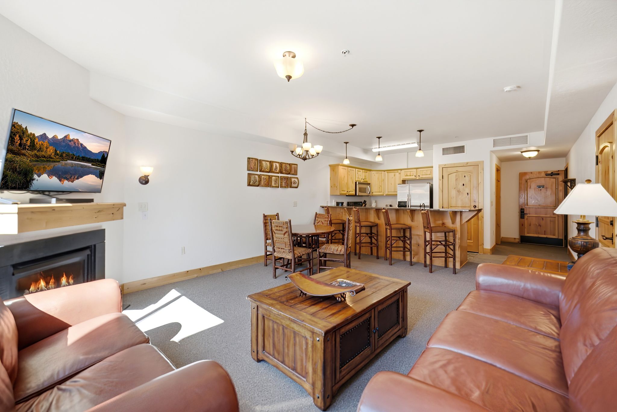 Open-concept living space featuring a built-in fireplace with a wood mantle, a full kitchen with light wood cabinetry and stainless steel appliances, a breakfast bar, and recessed lighting