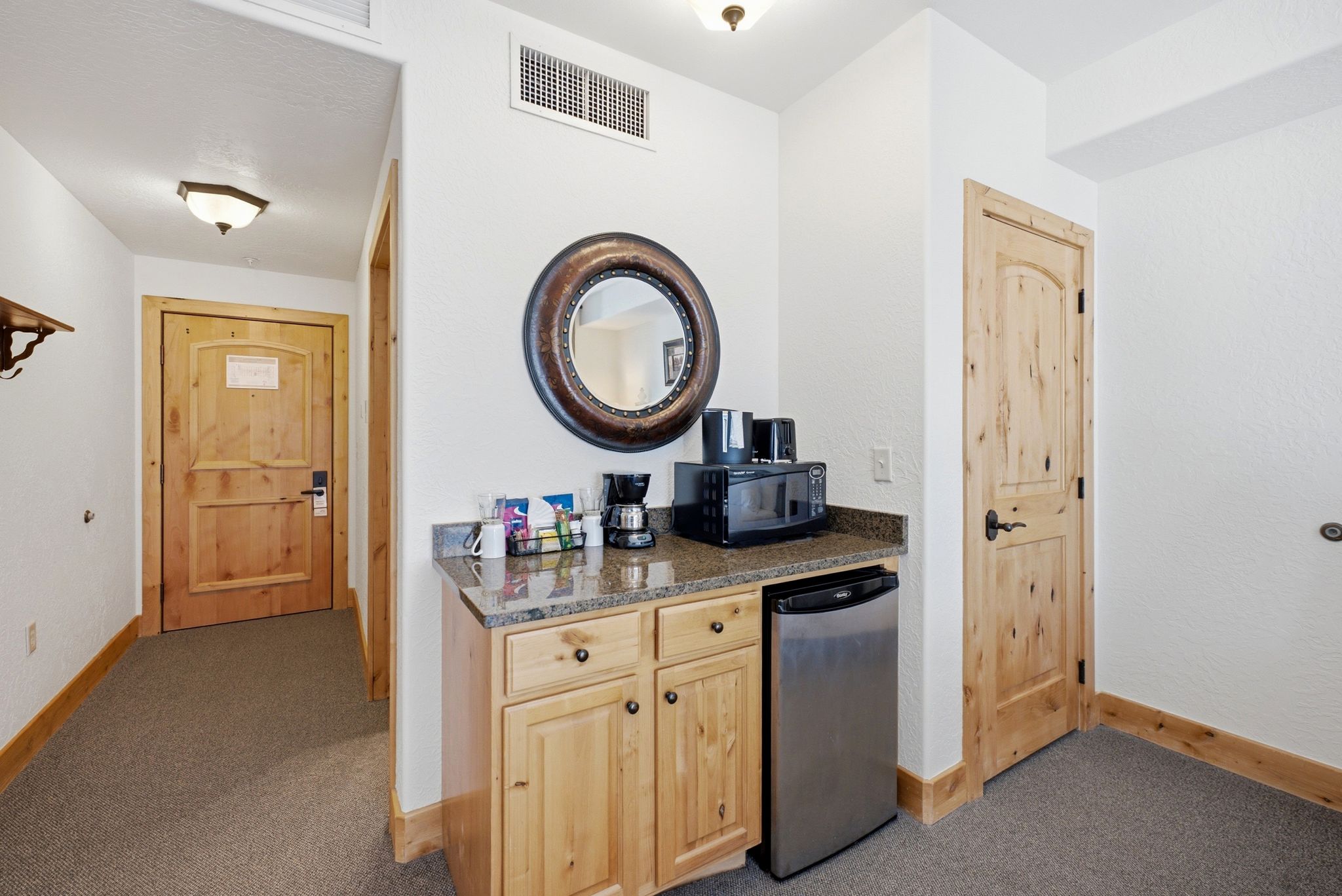 Compact kitchenette featuring light wood cabinetry, a stone-finish countertop, and a stainless steel under-counter refrigerator