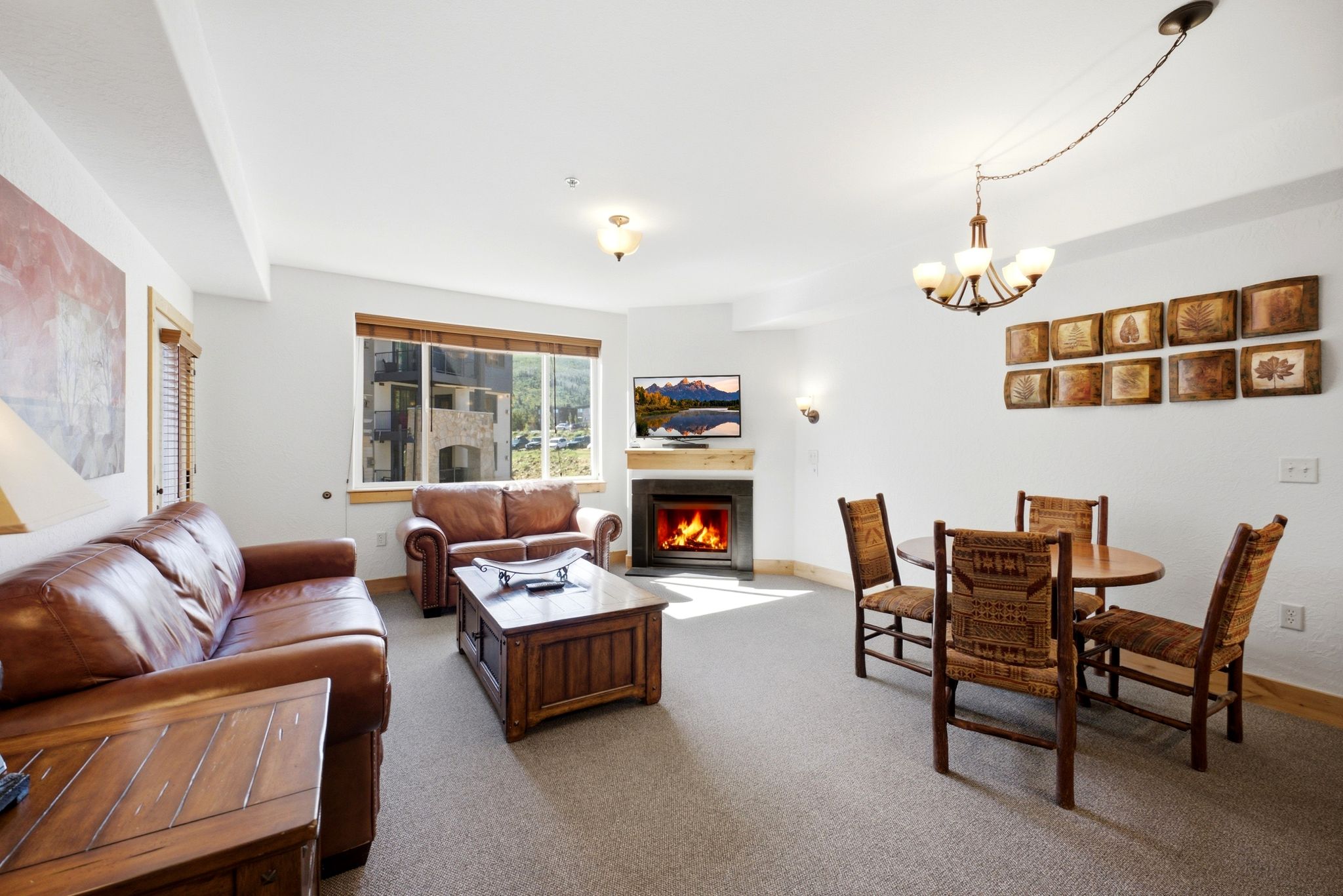 Open-concept living space with a built-in fireplace, wall-mounted television, and a four-person dining area featuring a chandelier