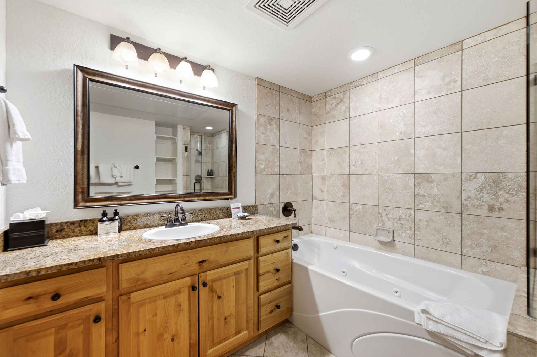 Bathroom featuring a spacious vanity with a granite-look countertop, wood-finish cabinetry, and an undermount sink