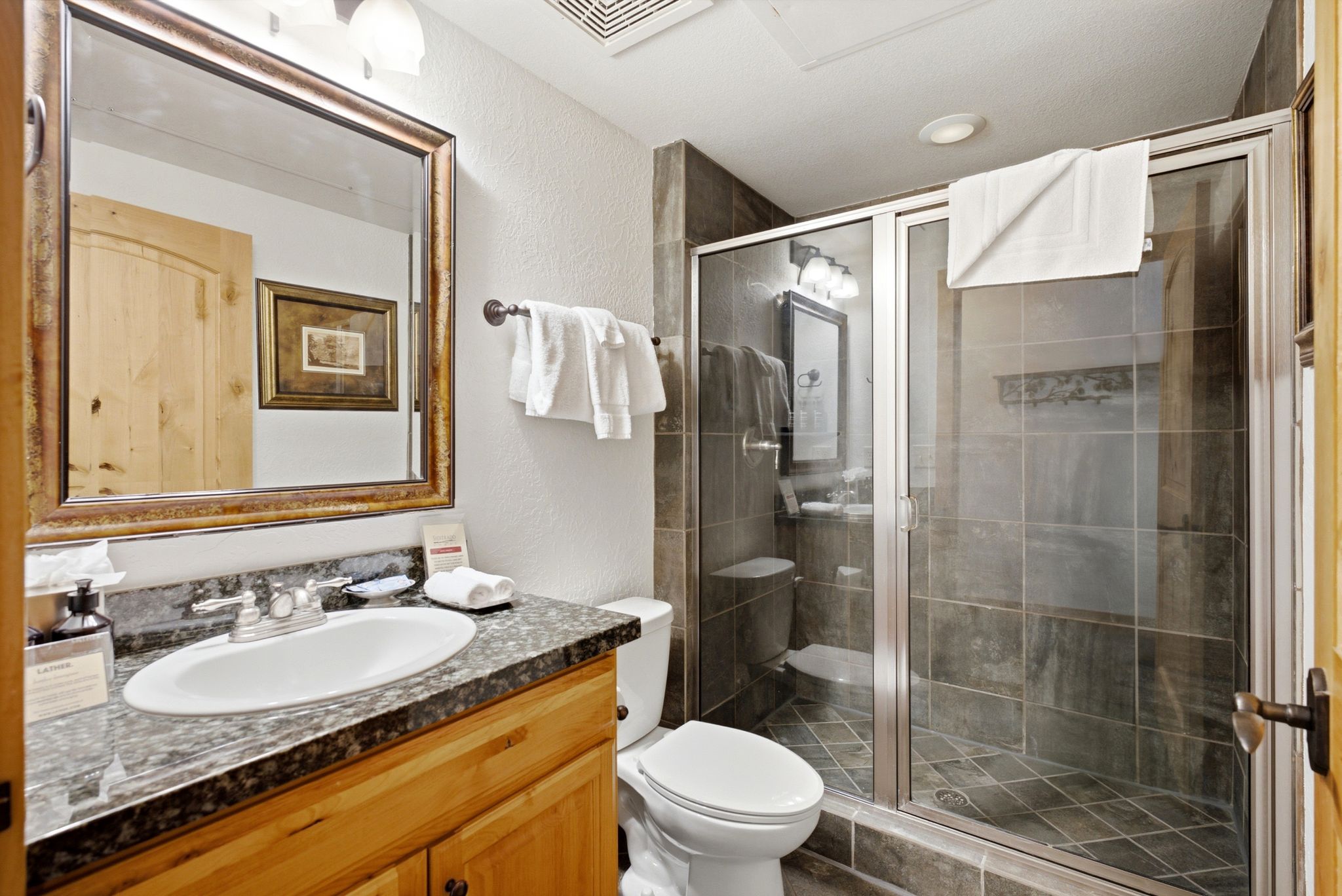 Bathroom featuring a wood-finish vanity with a granite-style countertop, an undermount sink, and a framed mirror