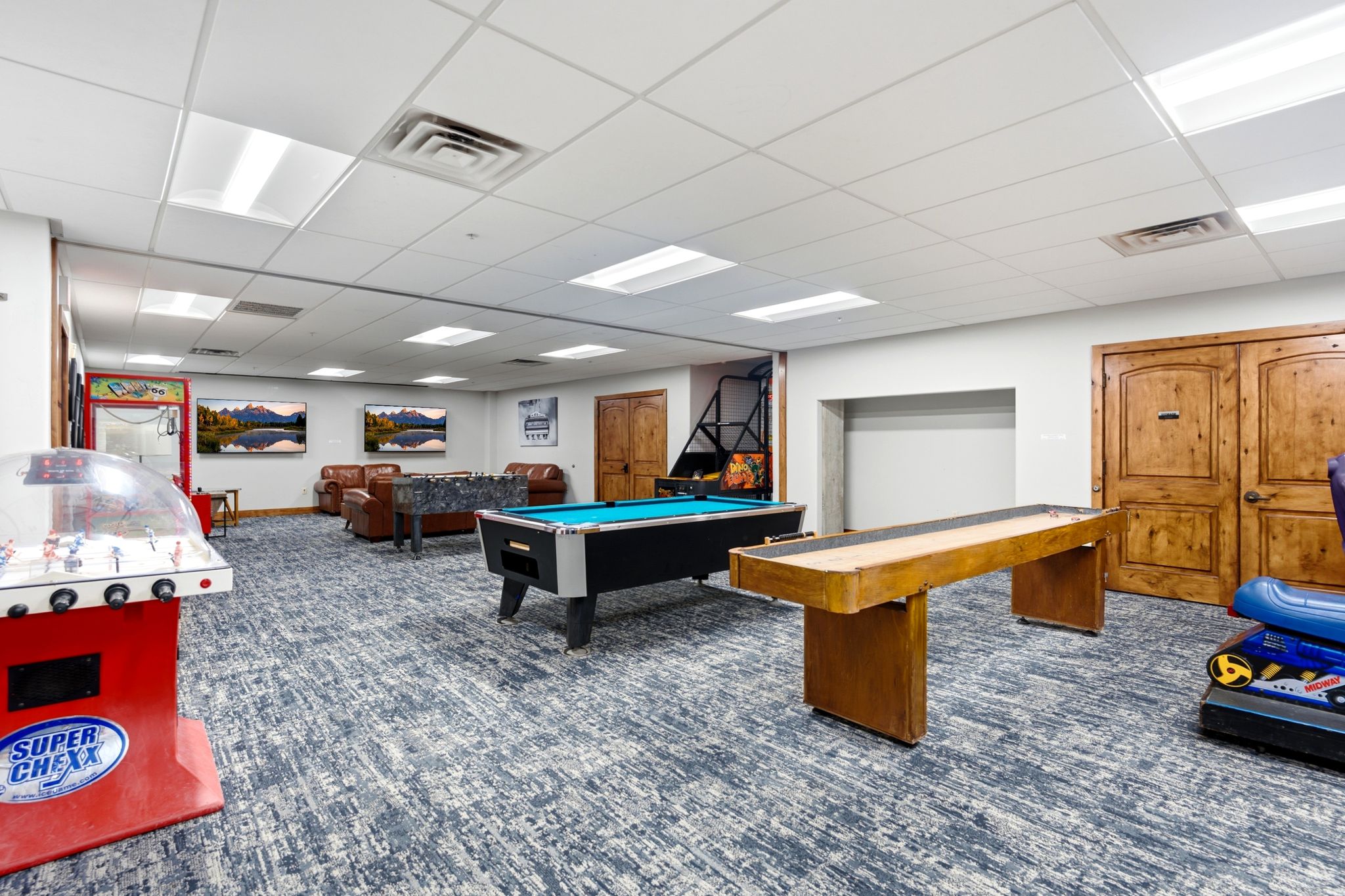 Spacious recreation room featuring patterned carpet flooring, recessed lighting, and wooden double doors